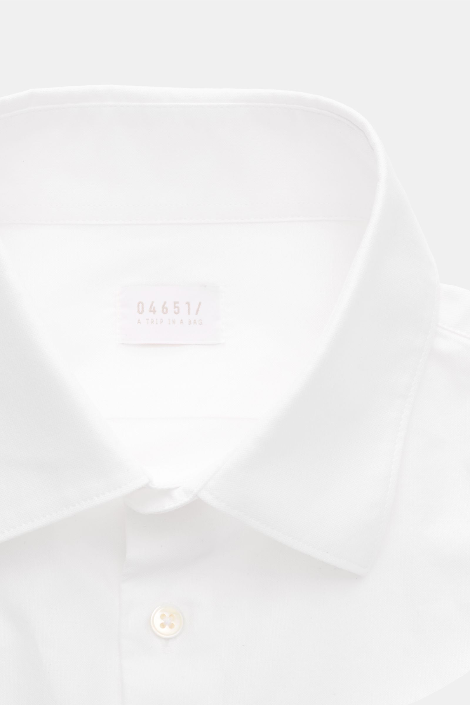 Close-up front view of the white 04651/ A trip in a bag Oxford-Hemd Kent-Kragen weiß showing the Kent collar, French placket, and a button. Dieses klassisch schlichte Oxford-Hemd mit Kent-Kragen von 04651/ A TRIP IN A BAG wurde aus reiner Baumwolle gef