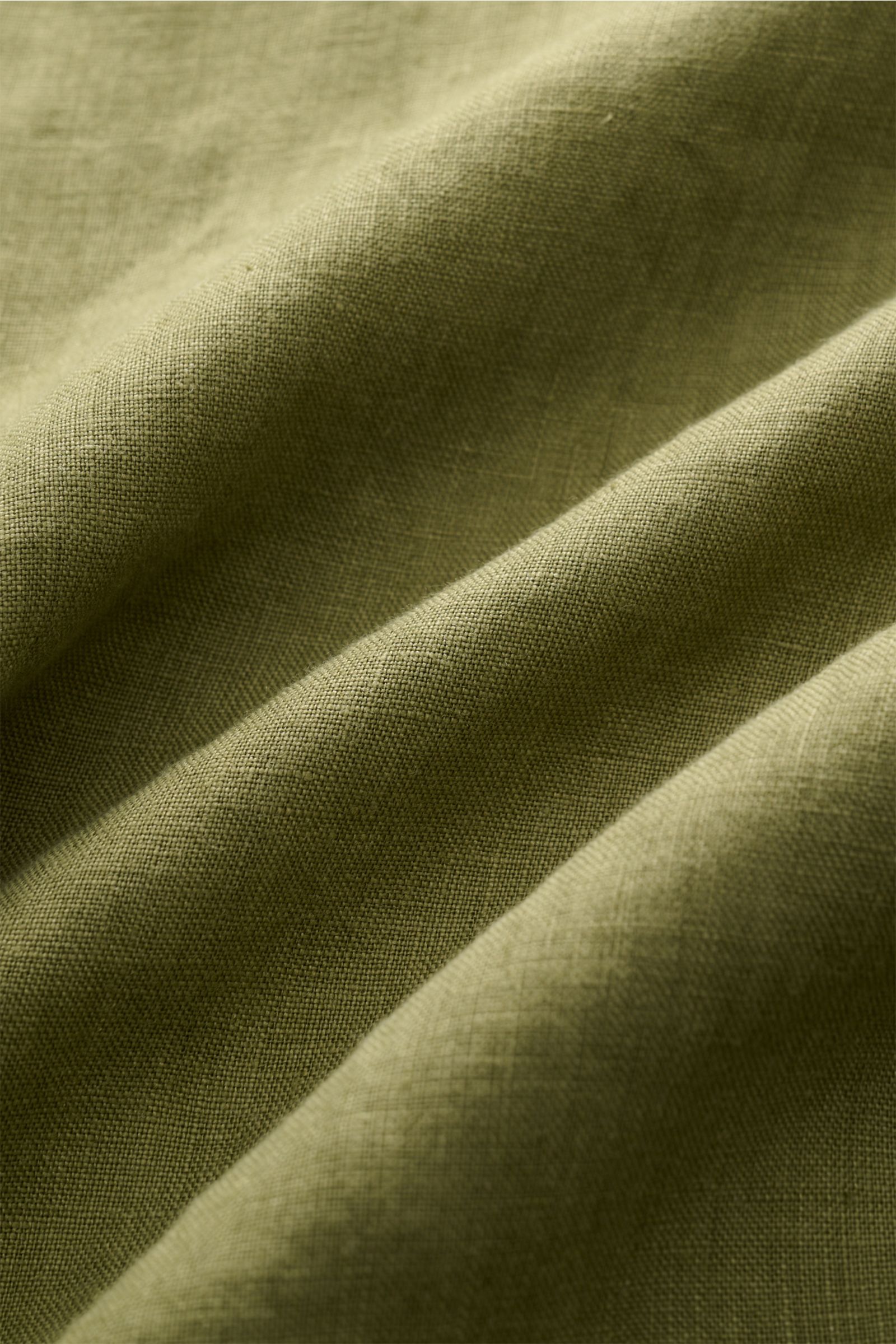 Close-up front view of olive green linen fabric showing fine texture and weave of the 04651/ A trip in a bag Leinenhemd Kent-Kragen oliv. Mühelose Leichtigkeit