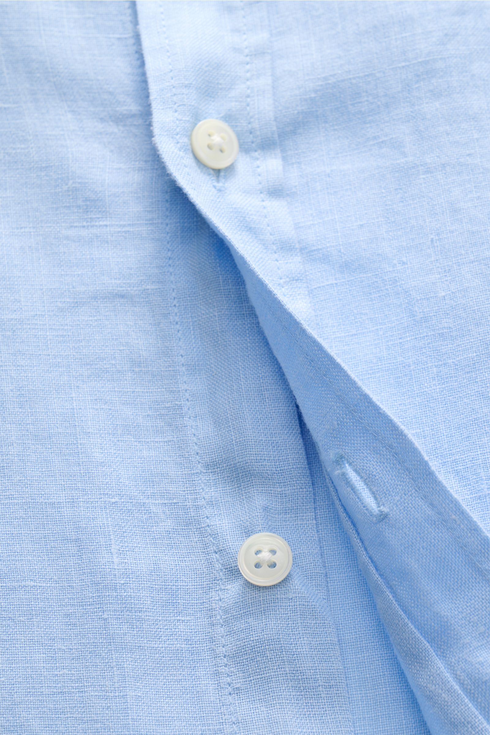 Close-up shot of the button placket and fabric texture of the 04651/ A trip in a bag Leinenhemd Kent-Kragen hellblau, a light blue pure linen shirt with airy, lightweight quality and classic details.

Mühelose 