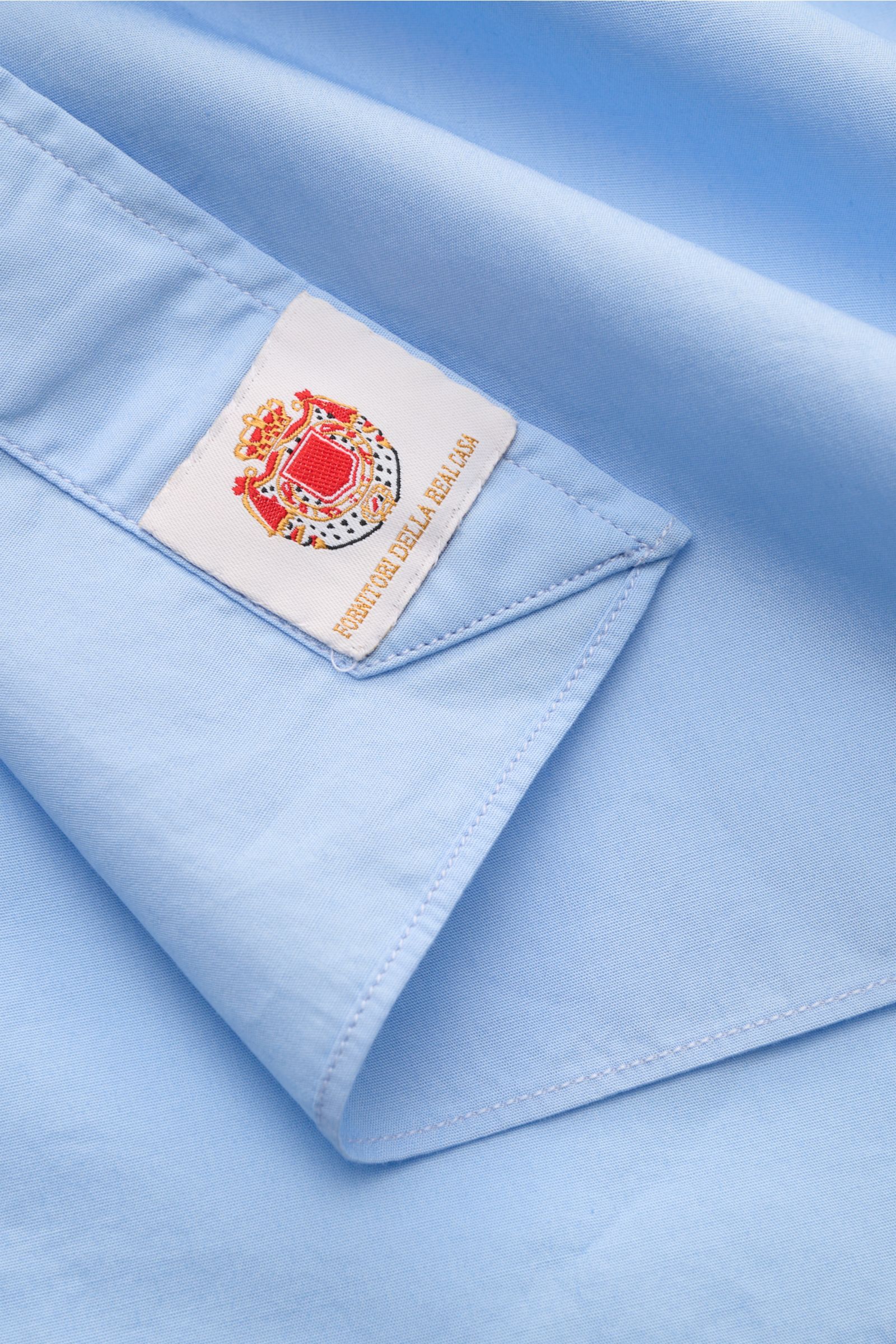 Close-up top-down view of the light blue Borrelli Casual Hemd 'Ettore' Haifisch-Kragen hellblau showing smooth poplin cotton fabric, slim fit, shark collar, French button placket with mother-of-pearl buttons, classic sport cuff, and rounded hem with label