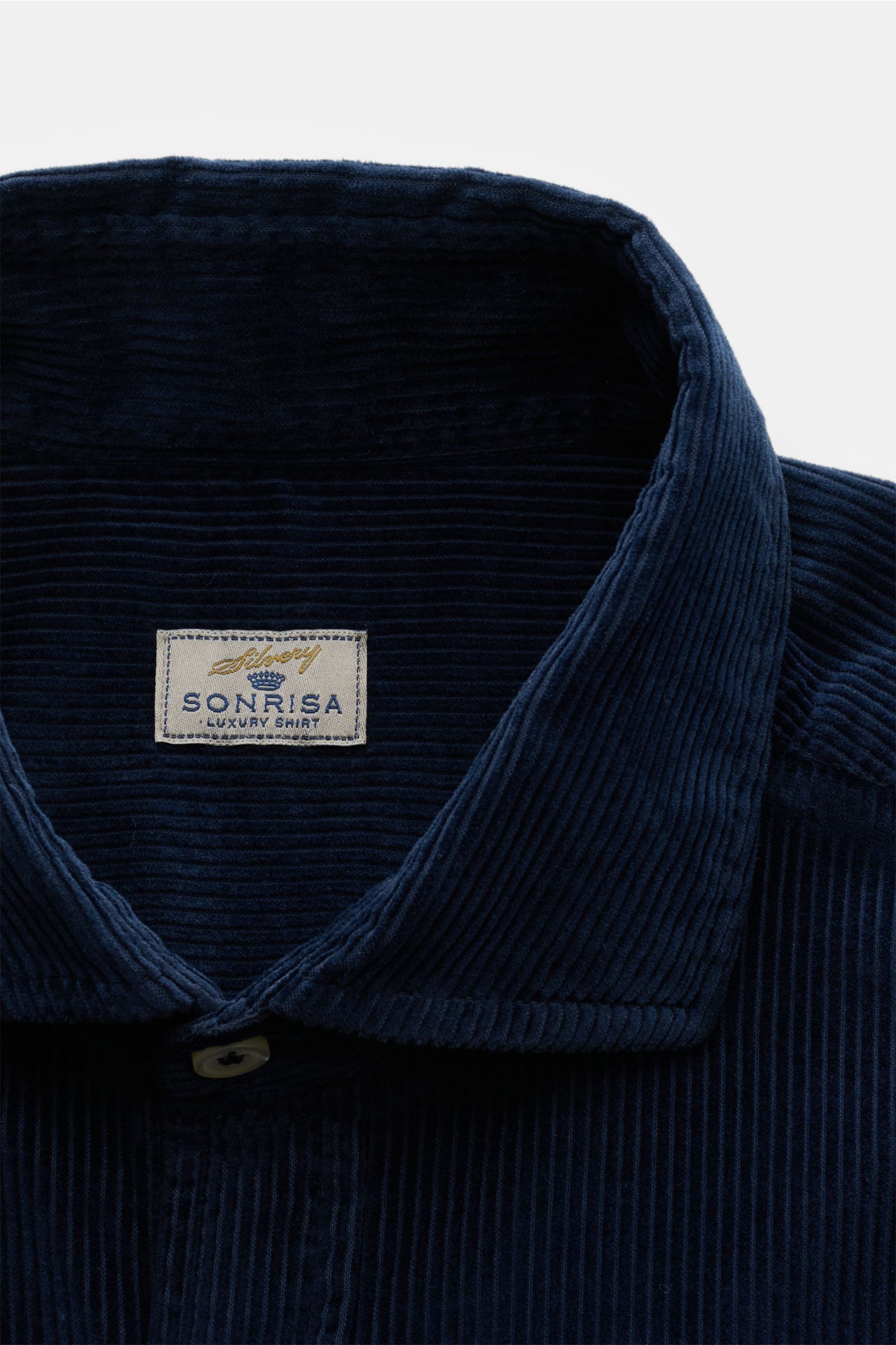 Nahaufnahme des Sonrisa Cordhemd Haifisch-Kragen navy aus weichem, warmem Baumwollcord, Slim Fit mit klassischem Haifisch-Kragen, aufgesetzter Knopfleiste und kleinem Weblabel am Saum, fotografiert von vorne oben. Leger durch Herbst und Winter.