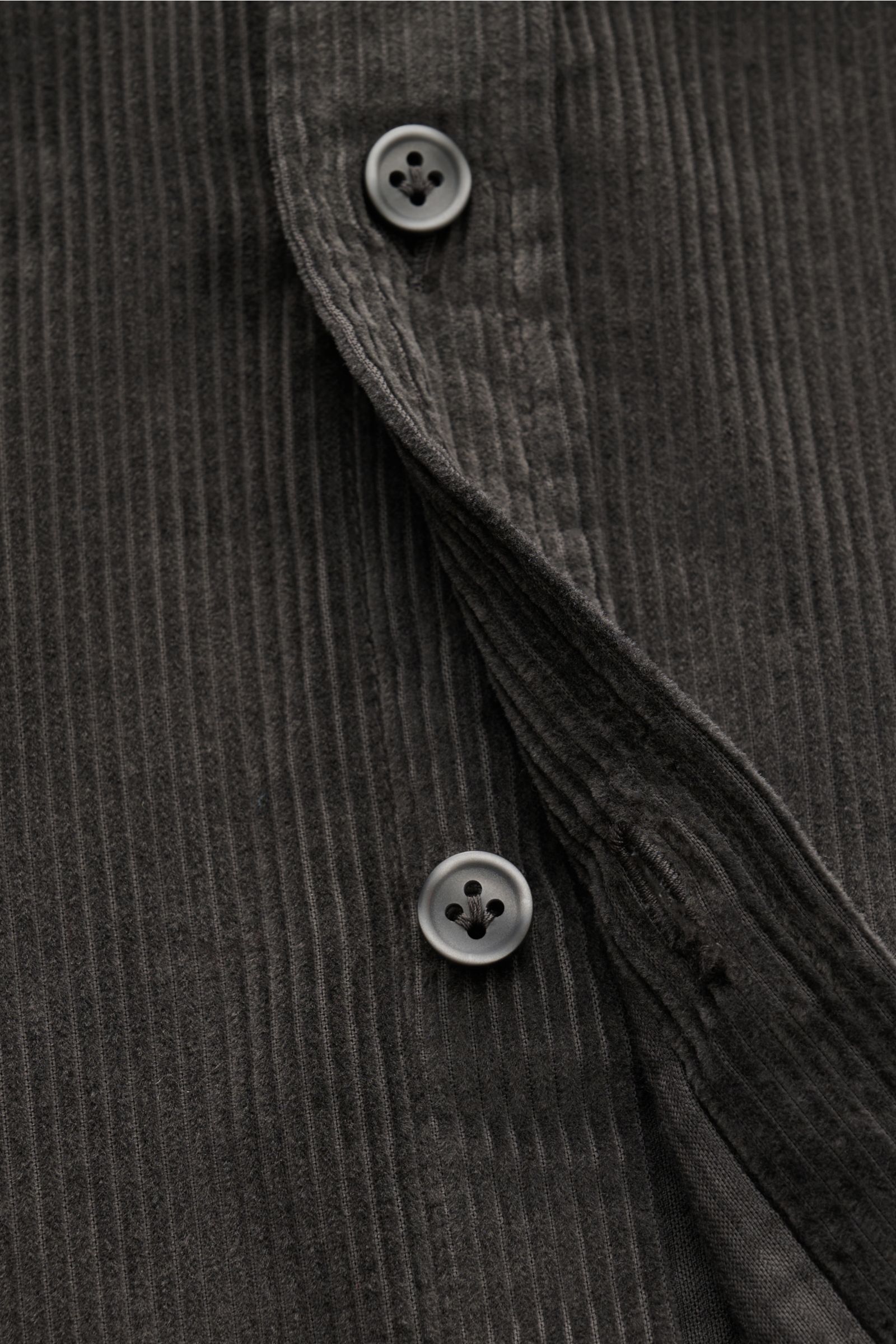 Nahaufnahme aus schräger Perspektive des Sonrisa Cordhemd Haifisch-Kragen dunkelgrau aus weichem Baumwollcord mit Knopfleiste und gerundetem Saum.