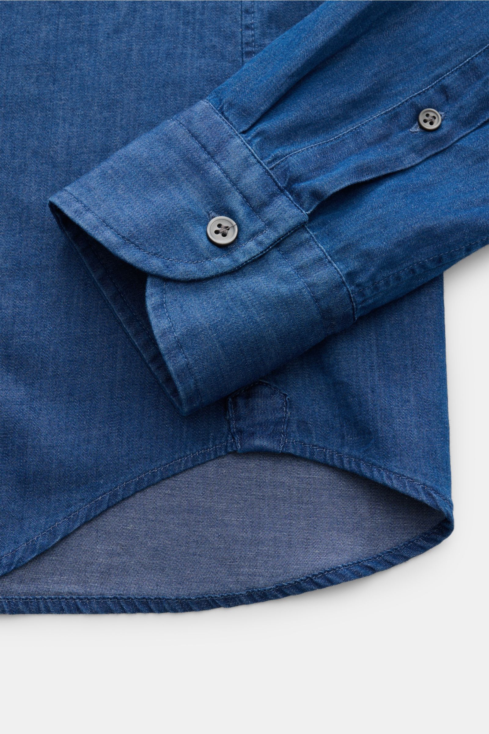 Nahaufnahme des Saumverlaufs und der klassisch sportlichen Manschette eines blauen Sonrisa Chambray-Hemd Haifisch-Kragen slim fit aus reiner Baumwolle.