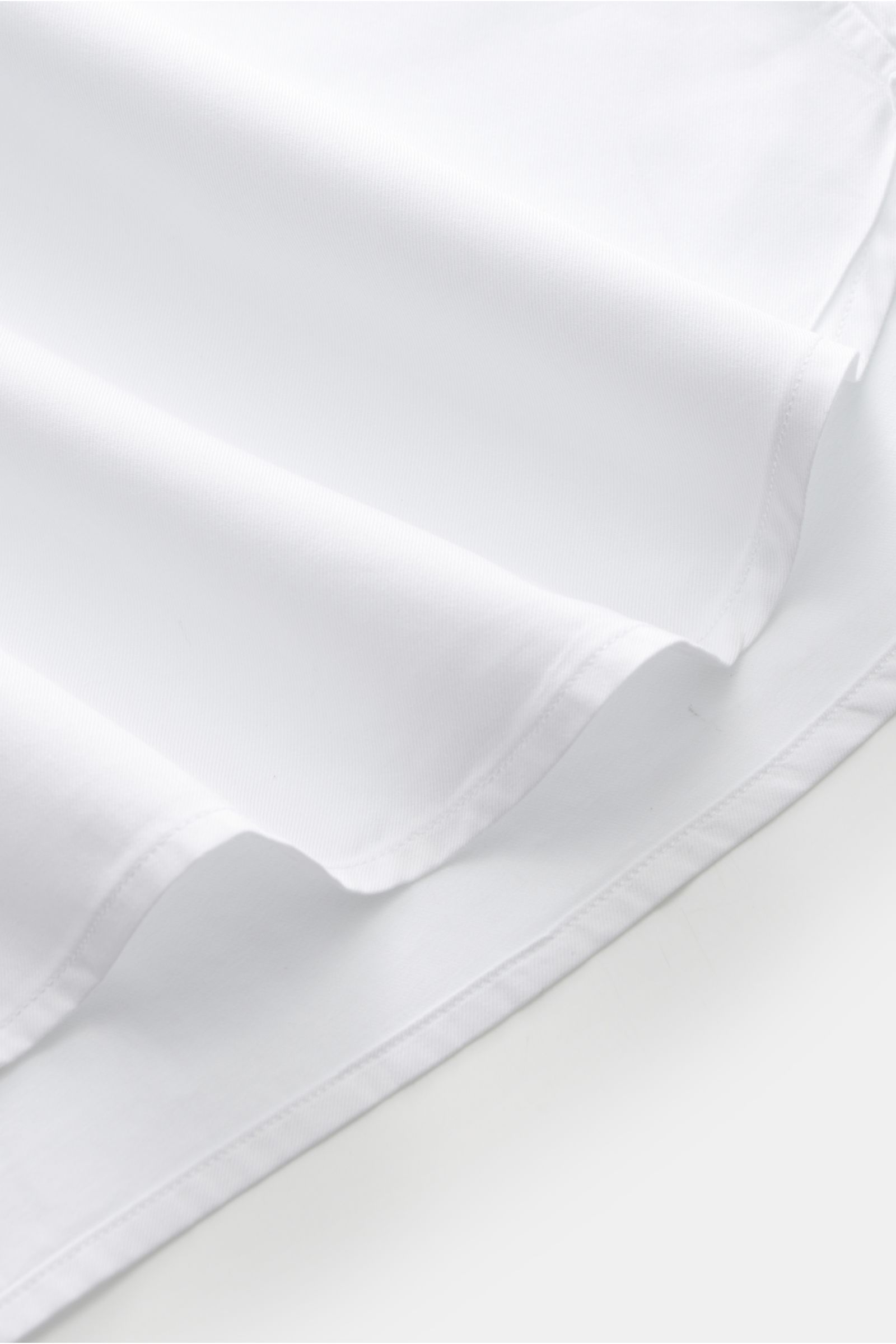 Close-up image of the hem of the Guglielminotti Casual Hemd Haifisch-Kragen weiß, photographed from a low side angle, showing twill aus reiner Baumwolle, weicher, glatter Griff, Regular Fit, Haifisch-Kragen, französische Knopfleiste, klassische Sportmansc