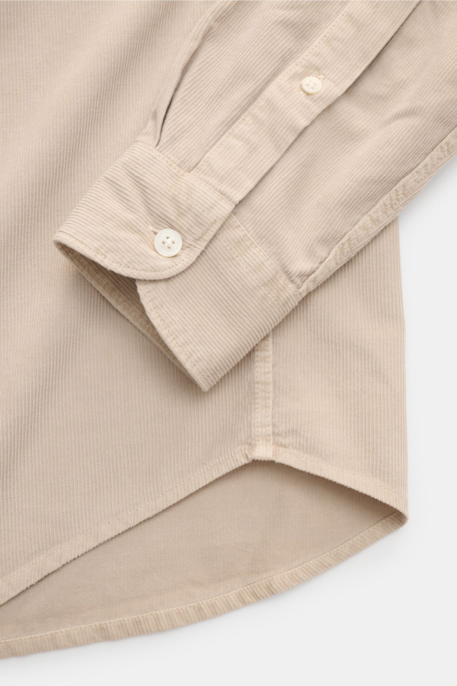 Closed Cordhemd Button-Down-Kragen beige showing a close-up of the shirt cuff and hem from a top-down perspective, highlighting soft, garment-dyed fine cotton corduroy with pearl buttons, tonal stitching, and a rounded hem, perfect for autumn urban looks.