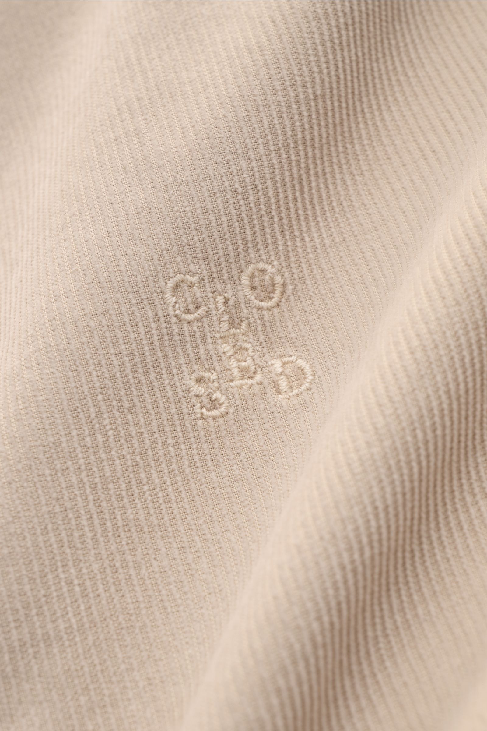 Close-up of the beige Closed Cordhemd Button-Down-Kragen showing the fine cord fabric texture and tonal embroidered logo, photographed from a frontal angle. Perfekt für den Herbst: Das stückgefärbte Feincord-Hemd von CLOSED verbindet warmen, soften Cor