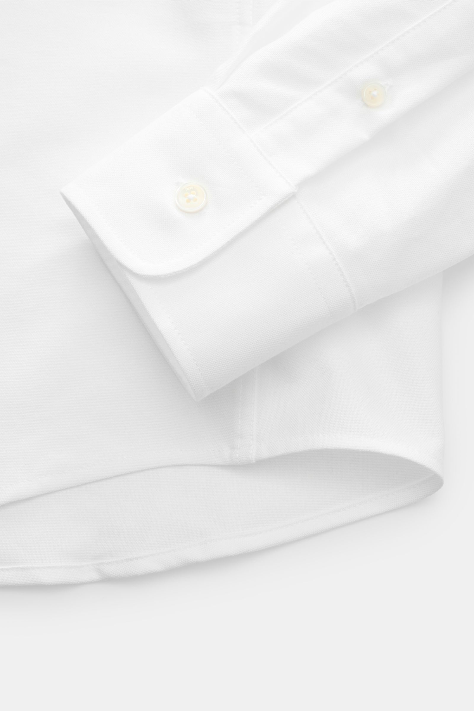 Nahaufnahme des weißen Ami Paris Oxford-Hemd Button-Down-Kragen im Oversize-Look, Fokus auf Ärmel mit klassischer Sportmanschette und gerundetem Saum, fotografiert von oben.