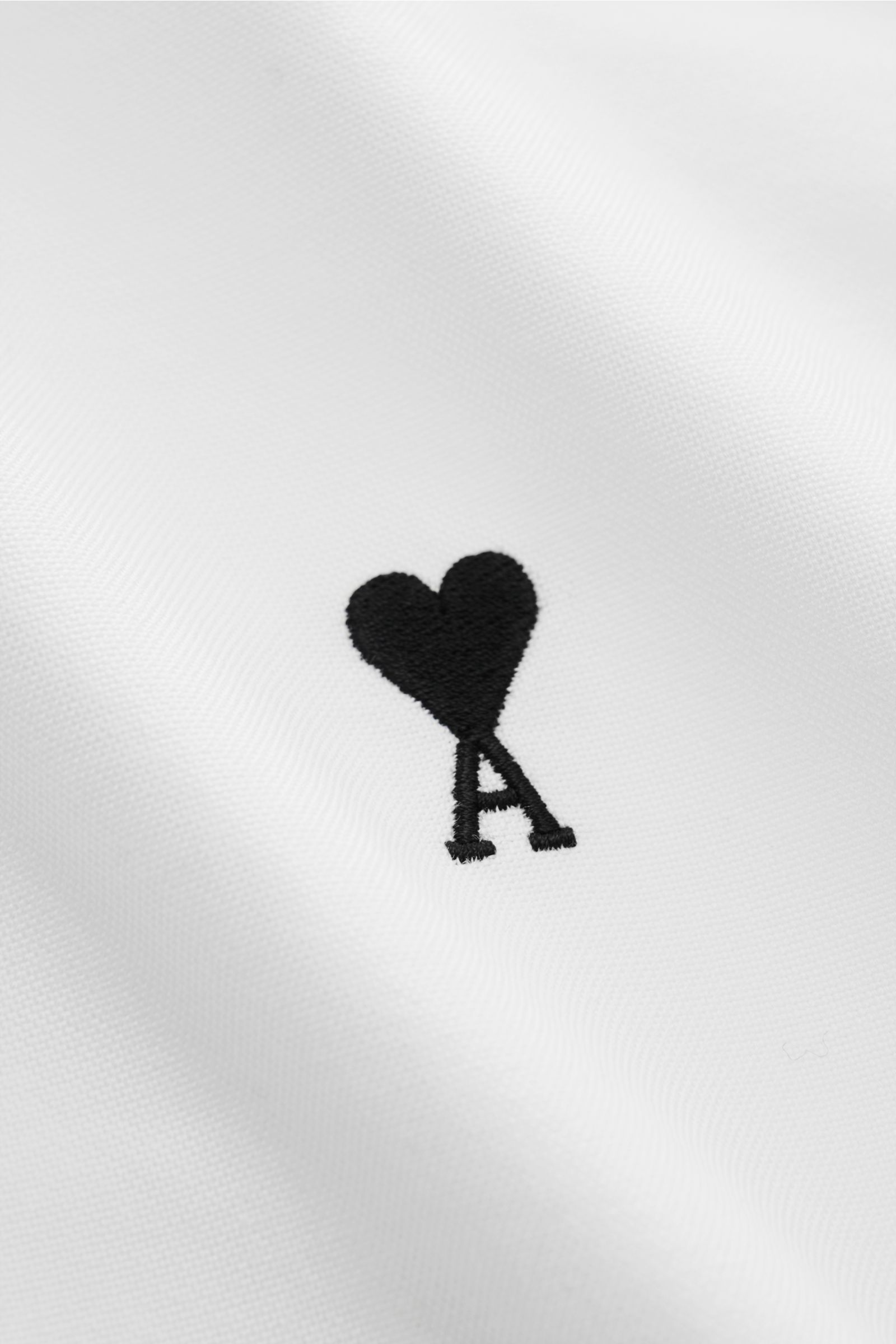 Nahaufnahme des Ami Paris Oxford-Hemd Button-Down-Kragen weiß mit sportlich-lässigem Oversize-Look, strukturierter Baumwolle und schwarzem Herz-A-Stick auf der Brust.