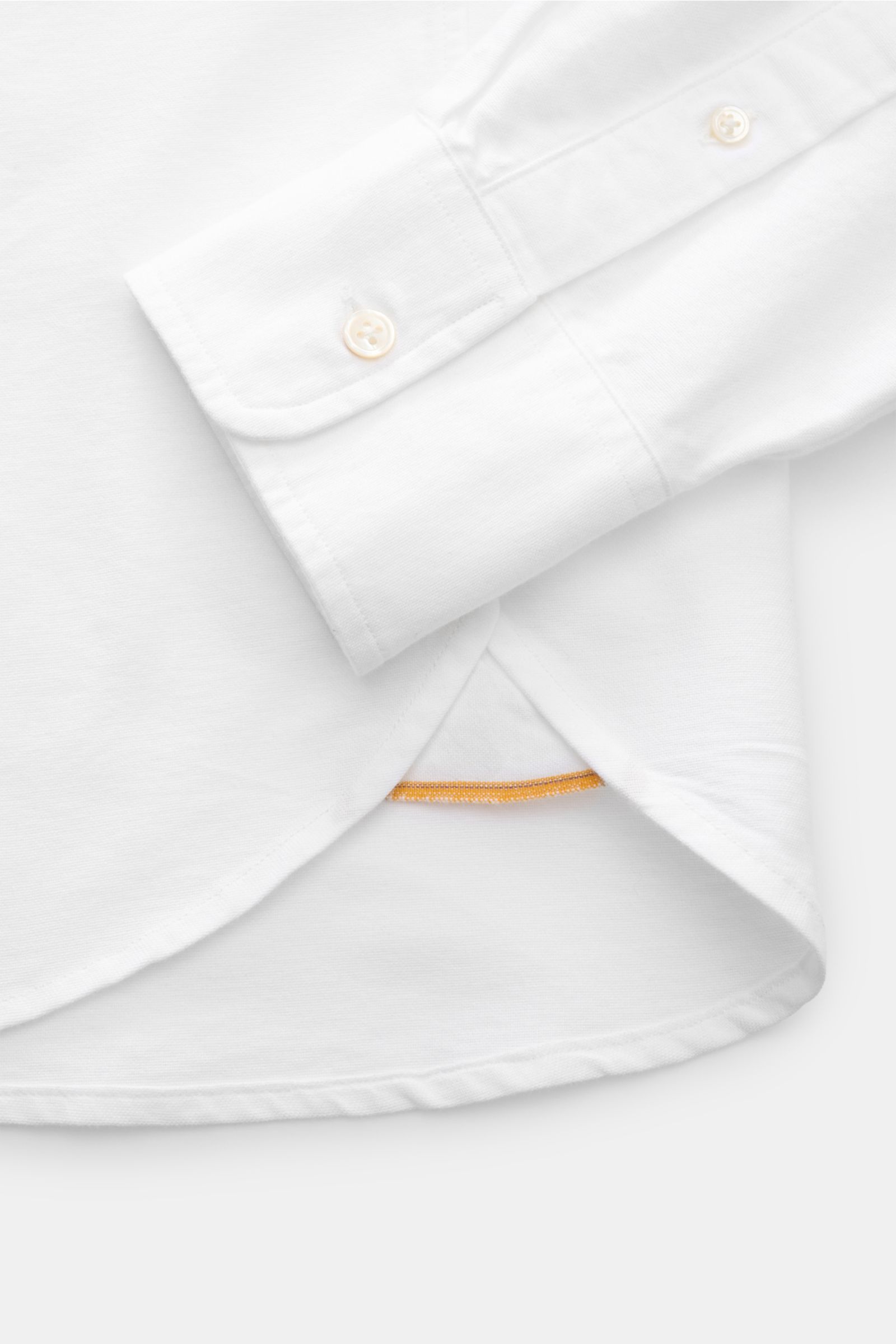 Close-up of the cuff and hem of the 04651/ A trip in a bag Oxford-Hemd Button-Down-Kragen weiß, showing button details and curved hem from a top-down perspective.

Description: Stilvoller Begleiter im Alltag: Das 'Handloomed Oxford Shirt' von 04651/ A 