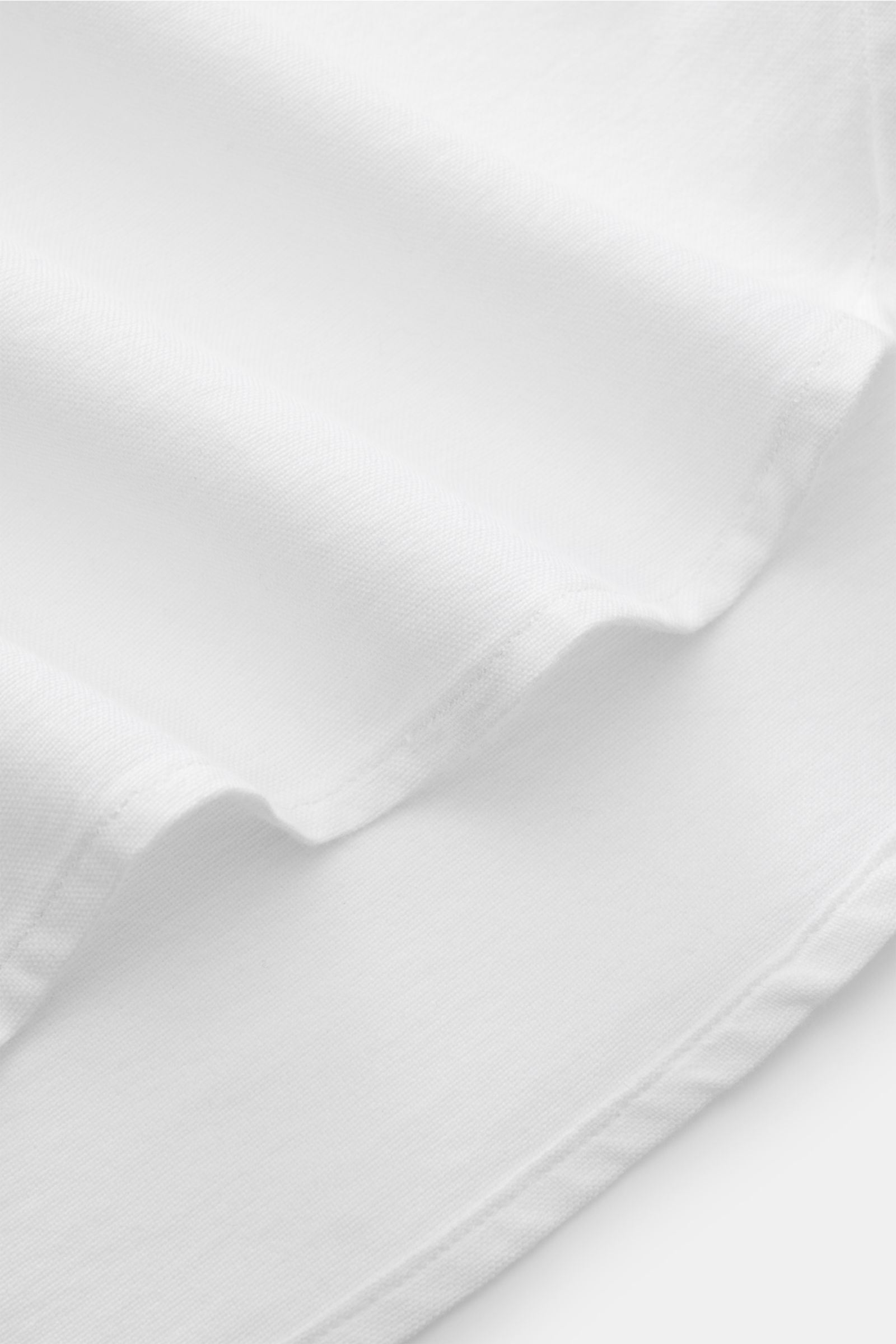 Close-up of the fabric and hem details of the 04651/ A trip in a bag Oxford-Hemd Button-Down-Kragen weiß, photographed from an angled top view, showing the finely woven 100% cotton material with a lightly textured feel and softly rounded hem edge. Stilvol