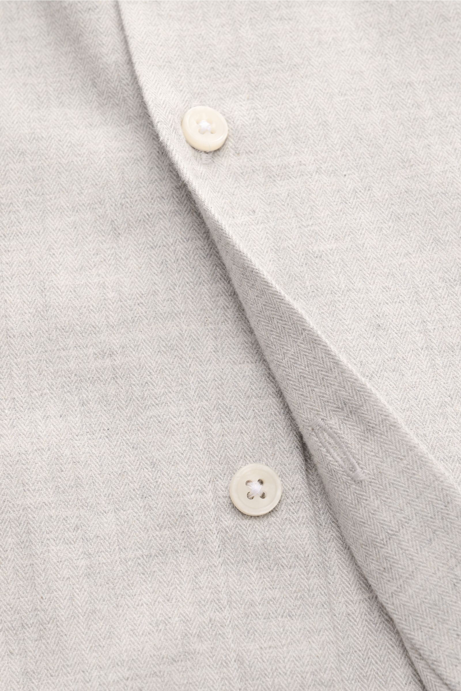 Nahaufnahme des BRAUN Hamburg Flanellhemds Haifisch-Kragen hellgrau meliert mit feinem Fischgrat aus Baumwolle, sehr weichem Griff, Slim Fit, französischer Knopfleiste, klassischer Sportmanschette und gerundetem Saumverlauf, von schräg oben fotografiert.