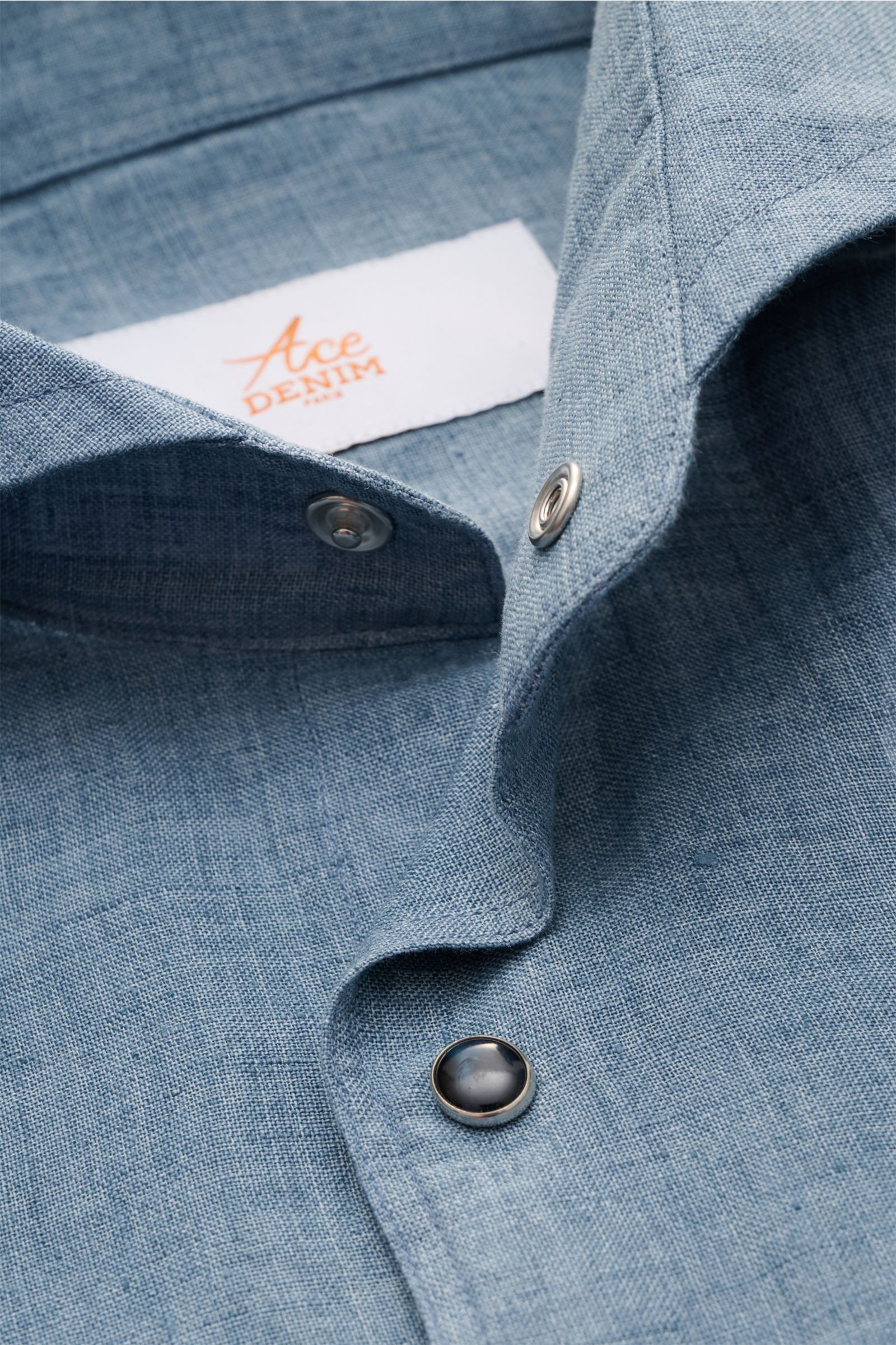 Close-up view of Ace Denim Linen shirt shark collar smoky blue, showing fabric texture, snap buttons, and label inside collar.

Stay comfortable in the warmer months: This ACE DENIM shirt in lightweight linen fabric is a casual statement piece for summ