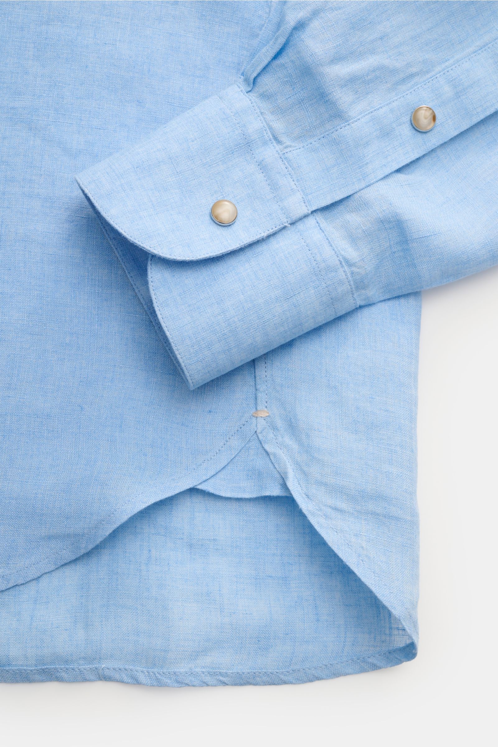 Close-up of the Ace Denim Linen shirt shark collar light blue showing the cuff and rounded hem from a top-down perspective, featuring pure linen, plain weave, lightweight fabric, visible yarn thickness fluctuations, slim fit, French button placket with sn
