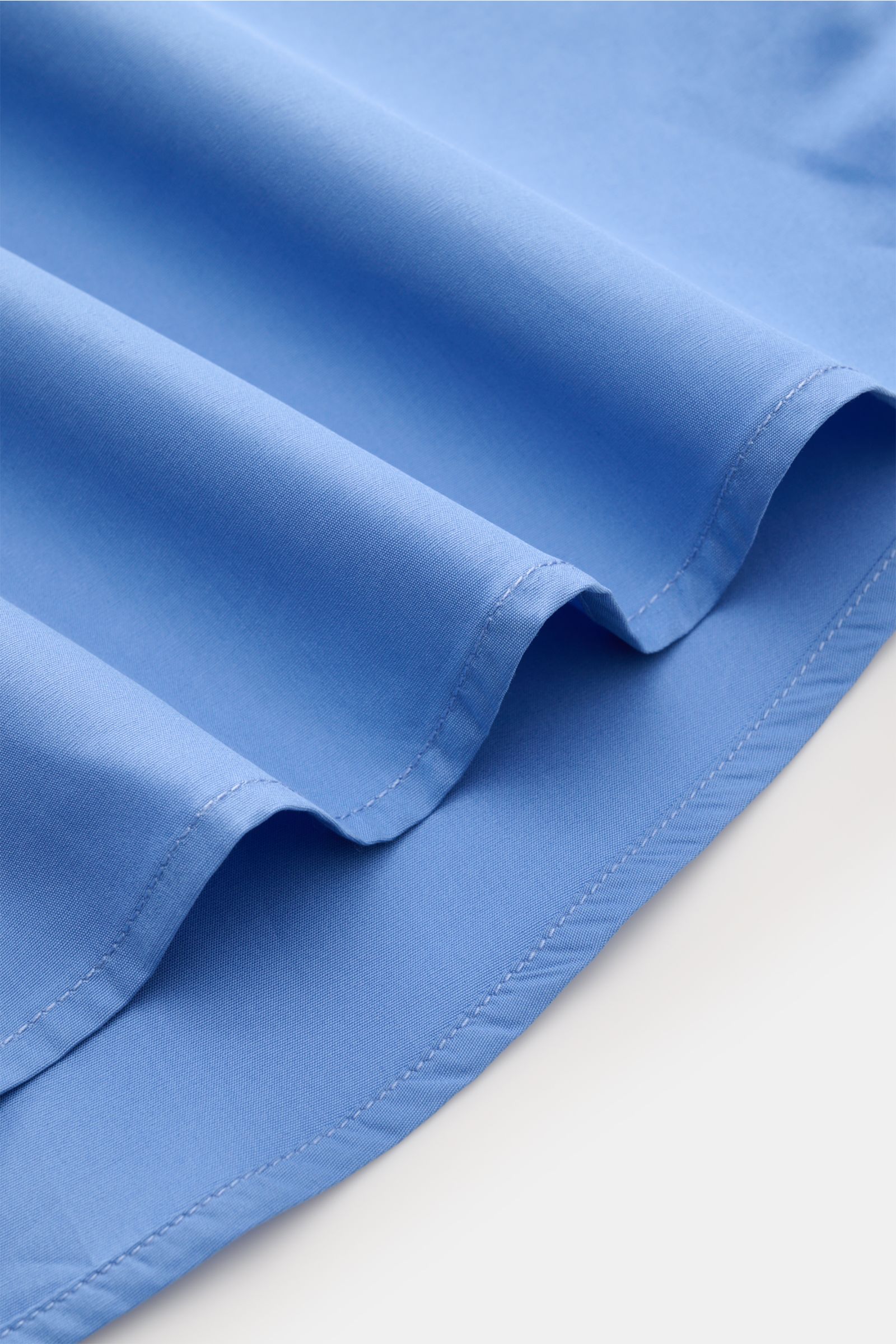 Close-up from the side of the slightly rounded hem of the A.P.C. Casual shirt Kent collar blue, made of pure cotton with smooth feel.