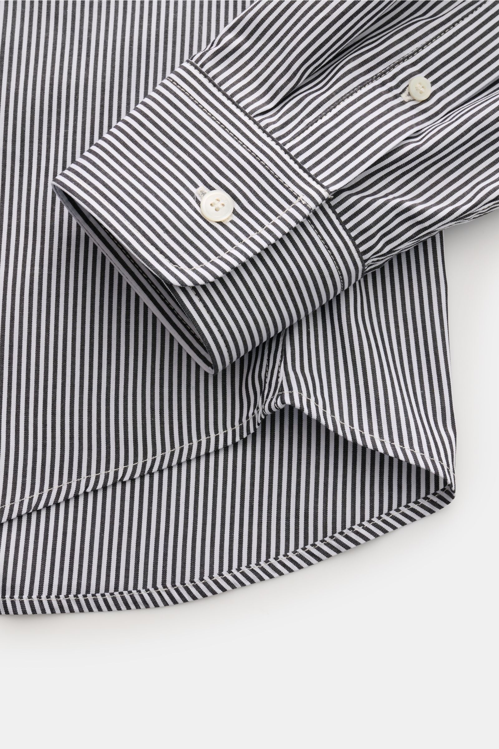 Close-up from above of the A.P.C. Casual Hemd Kent-Kragen schwarz/weiß gestreift showing the black and white striped cuff, button, and slightly rounded hem, made of pure cotton with a smooth feel, oversized fit, Kent collar, sewn-on button placket, classi