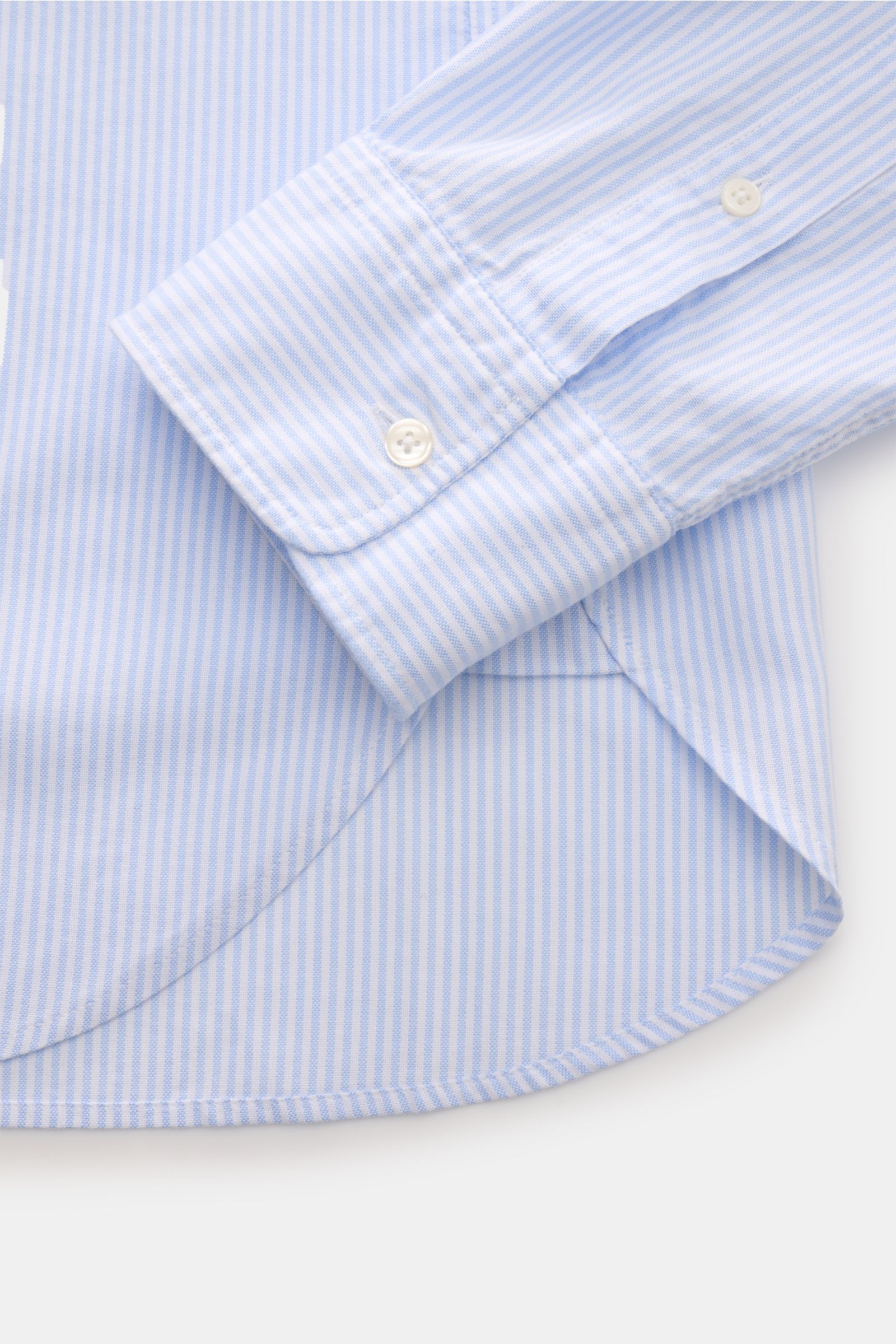 Close-up side view of Officine Générale Oxford-Hemd Button-Down-Kragen weiß/hellblau gestreift showing soft cotton fabric, buttoned cuff, chest pocket, and slightly rounded hem.

Zeitloses Essential: Das Oxford-Hemd von OFFICINE GÉNÉRALE überzeugt mit 