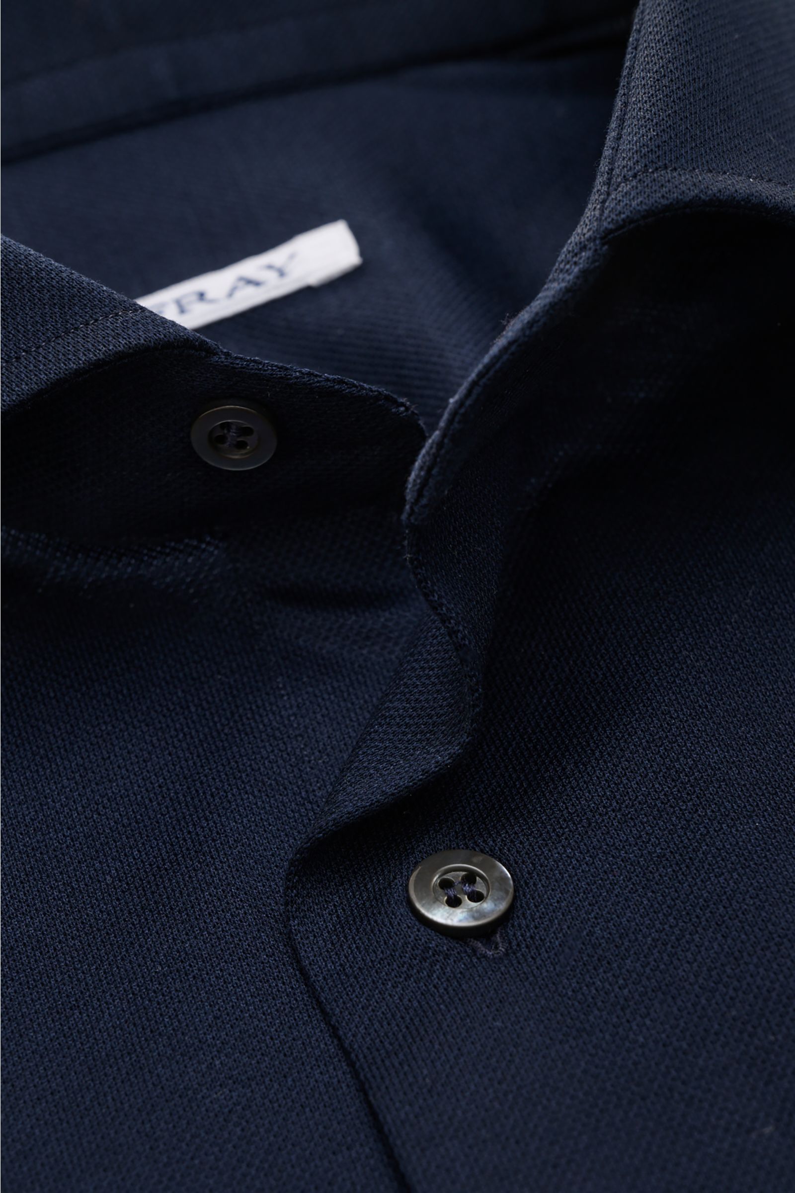 Close-up front view of the Fray Piqué-Hemd Haifisch-Kragen 'Lione Cucitura' navy shirt showing the textured cotton piqué fabric and buttons.

FRAY überzeugt mit dem Hemd 'Lione Cucitura' aus luftigem Piqué, gefertigt aus reiner Baumwolle – ein zeitlose