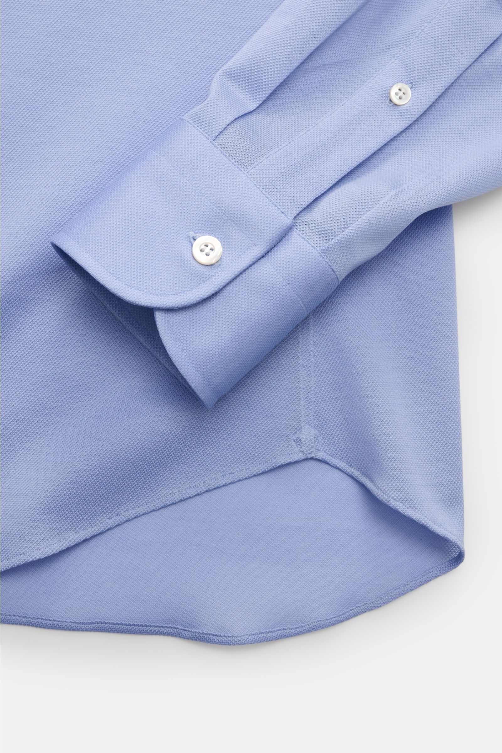 Close-up image from above of the cuff and hem of the Fray Piqué-Hemd Haifisch-Kragen 'Lione Cucitura' hellblau, made from airy pure cotton piqué with a slightly textured feel, slim fit, shark collar, classic sport cuff, back waist darts, and a gently roun