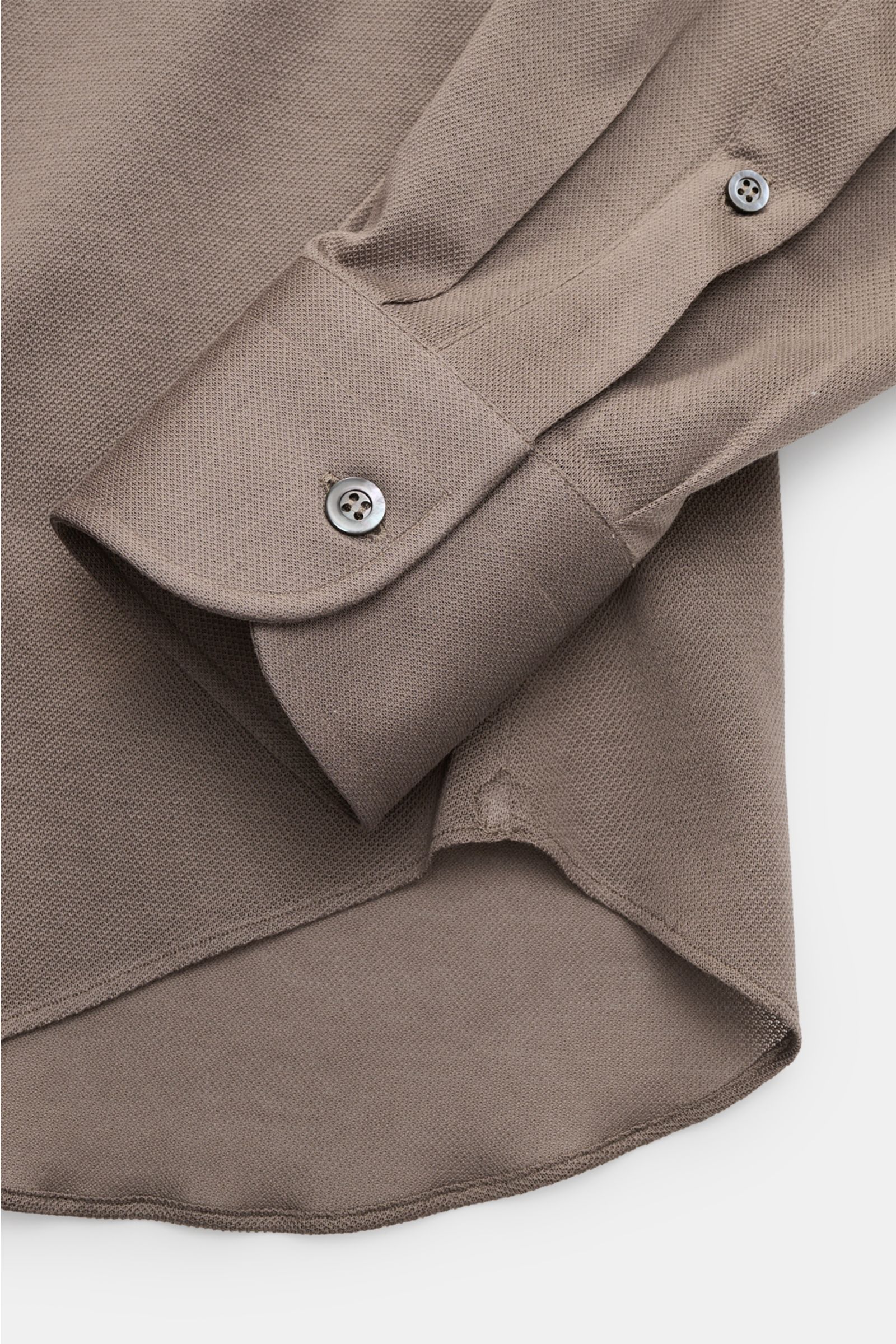 Close-up view of the sleeve and hem of the Fray Piqué-Hemd Haifisch-Kragen 'Lione Cucitura' graubraun, showing the textured piqué cotton fabric, slim fit cut, shark collar, classic sport cuff with button, back waist darts, and slightly rounded hem.

FR