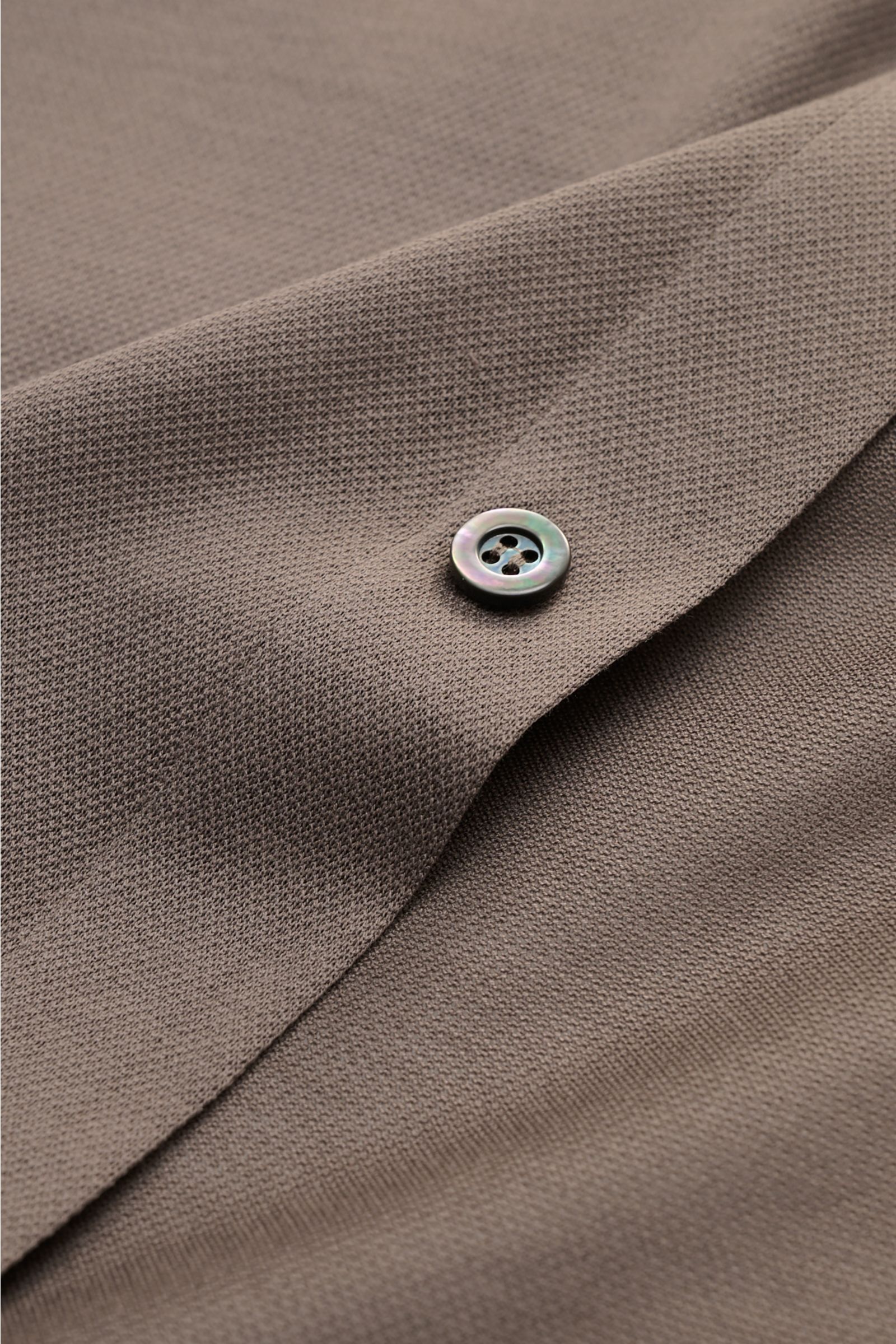 Close-up image of the Fray Piqué-Hemd Haifisch-Kragen 'Lione Cucitura' graubraun showing textured gray-brown piqué fabric and a single button. FRAY überzeugt mit dem Hemd 'Lione Cucitura' aus luftigem Piqué, gefertigt aus reiner Baumwolle – ein zeitlos