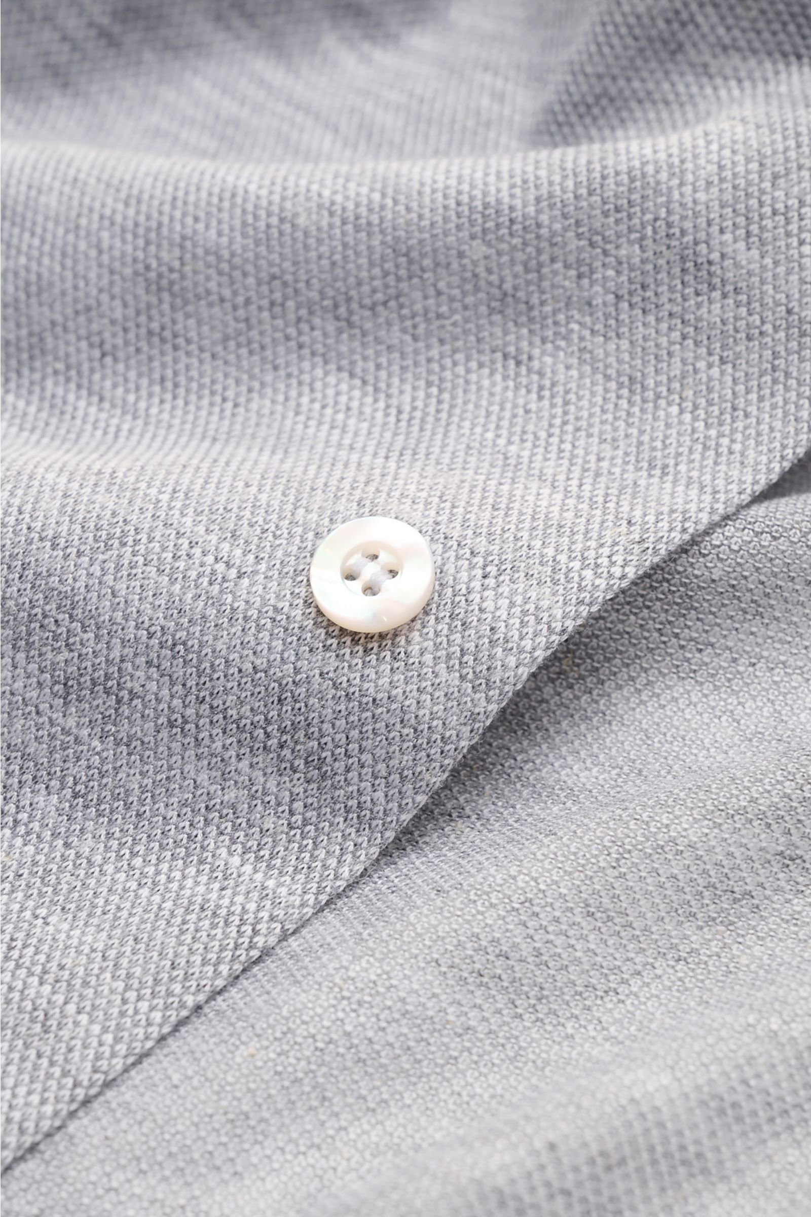 Close-up image of the Fray Piqué-Hemd Haifisch-Kragen 'Lione Cucitura' grau meliert showing fine grey melange piqué fabric and a white button from a top-down perspective. FRAY überzeugt mit dem Hemd 'Lione Cucitura' aus luftigem Piqué, gefertigt aus re