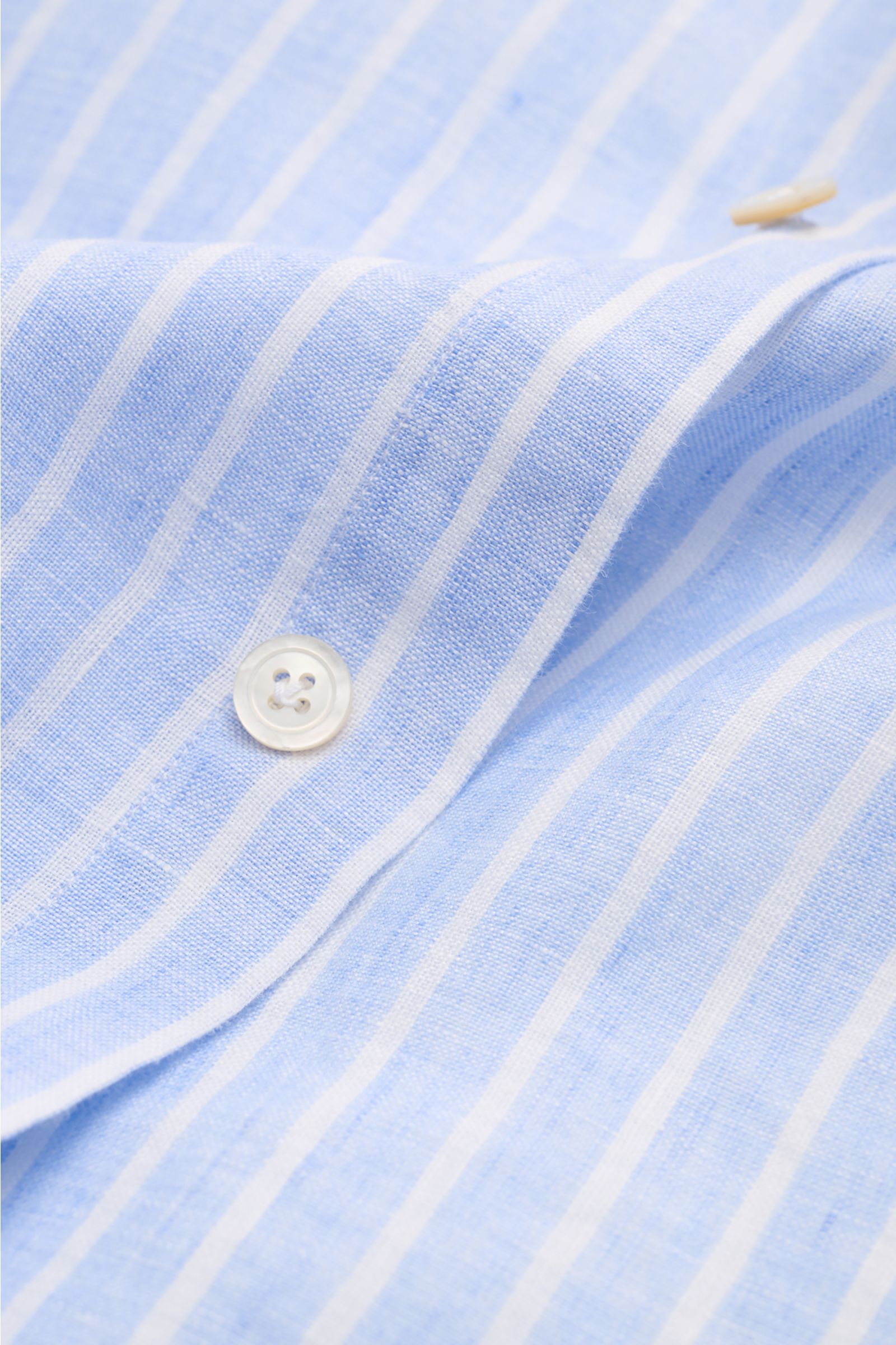 Close-up, top-down view of the Finamore Linen shirt 'Sergio Gaeta' shark collar light blue/white striped showing fabric texture and a white button.

Stylish summer essential: The lightweight linen shirt 'Sergio Gaeta' by FINAMORE works with a smart-cas