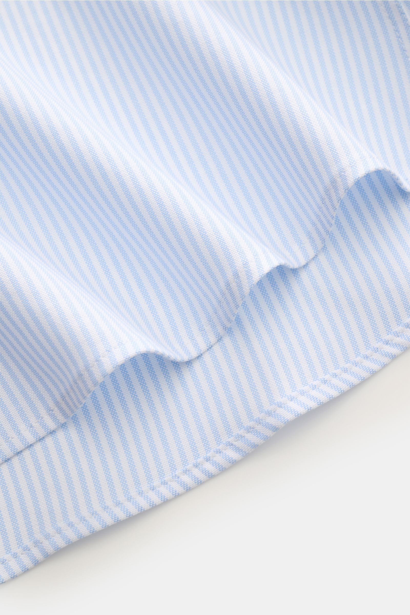 Ami Paris Oxford-Hemd Button-Down-Kragen hellblau/weiß gestreift, Oversize, aus reiner Baumwolle, Detailaufnahme des gerundeten Saumverlaufs im leichten Strukturgriff.