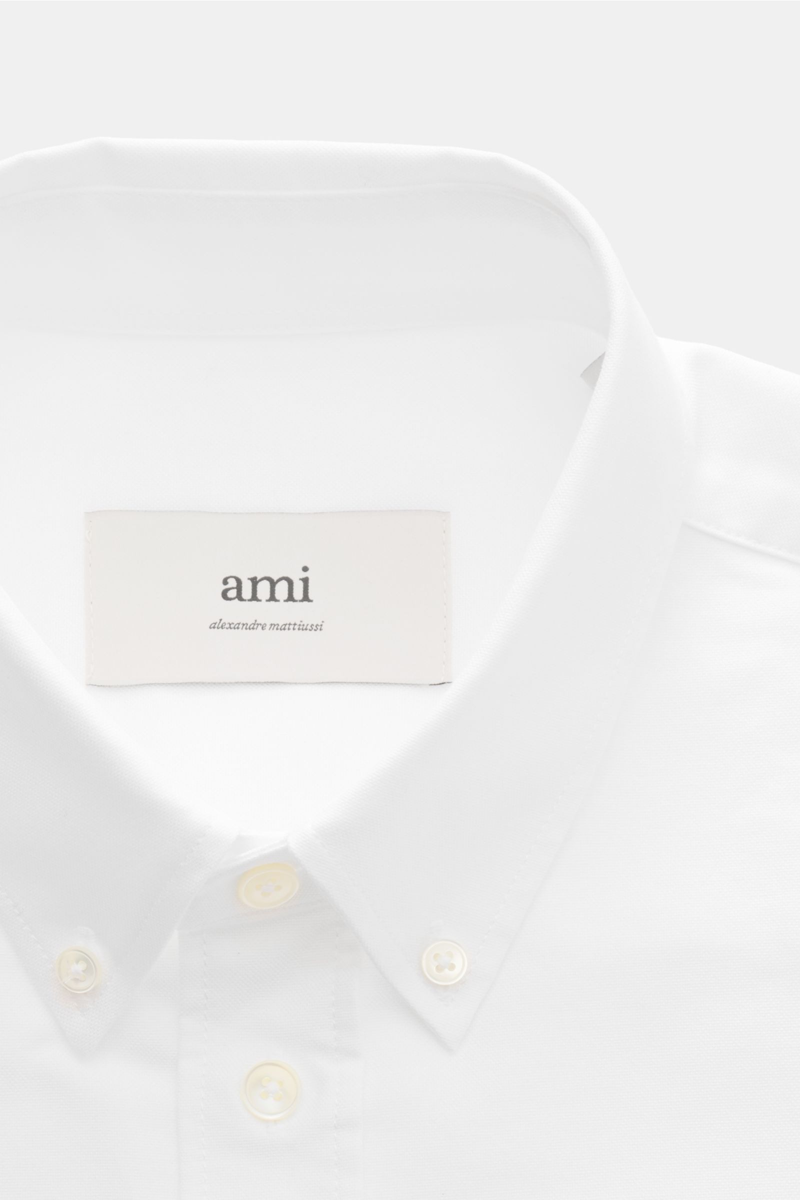 Ami Paris Oxford shirt button-down collar white shown from a close-up front perspective, highlighting the button-down collar, mother-of-pearl buttons, and signature heart stitching. For relaxed casual styles and more formal looks: This elegant shirt from 