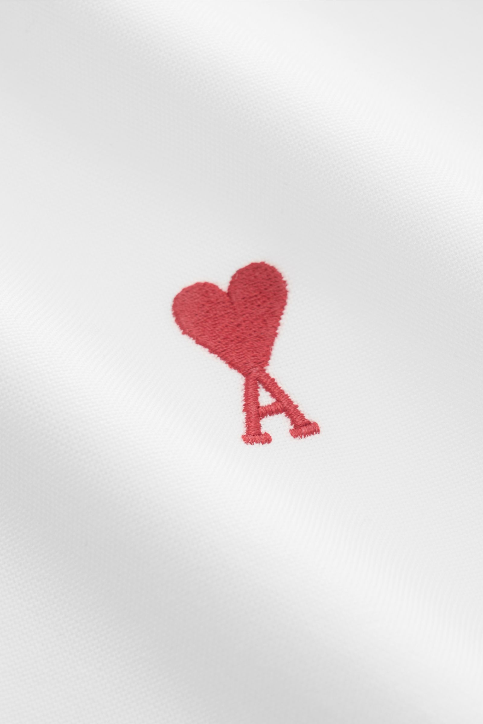Close-up front view of the red heart stitching with letter 'A' on white Ami Paris Oxford shirt button-down collar white, pure cotton Oxford fabric.

Description: For relaxed casual styles and more formal looks: This elegant shirt from AMI PARIS with si