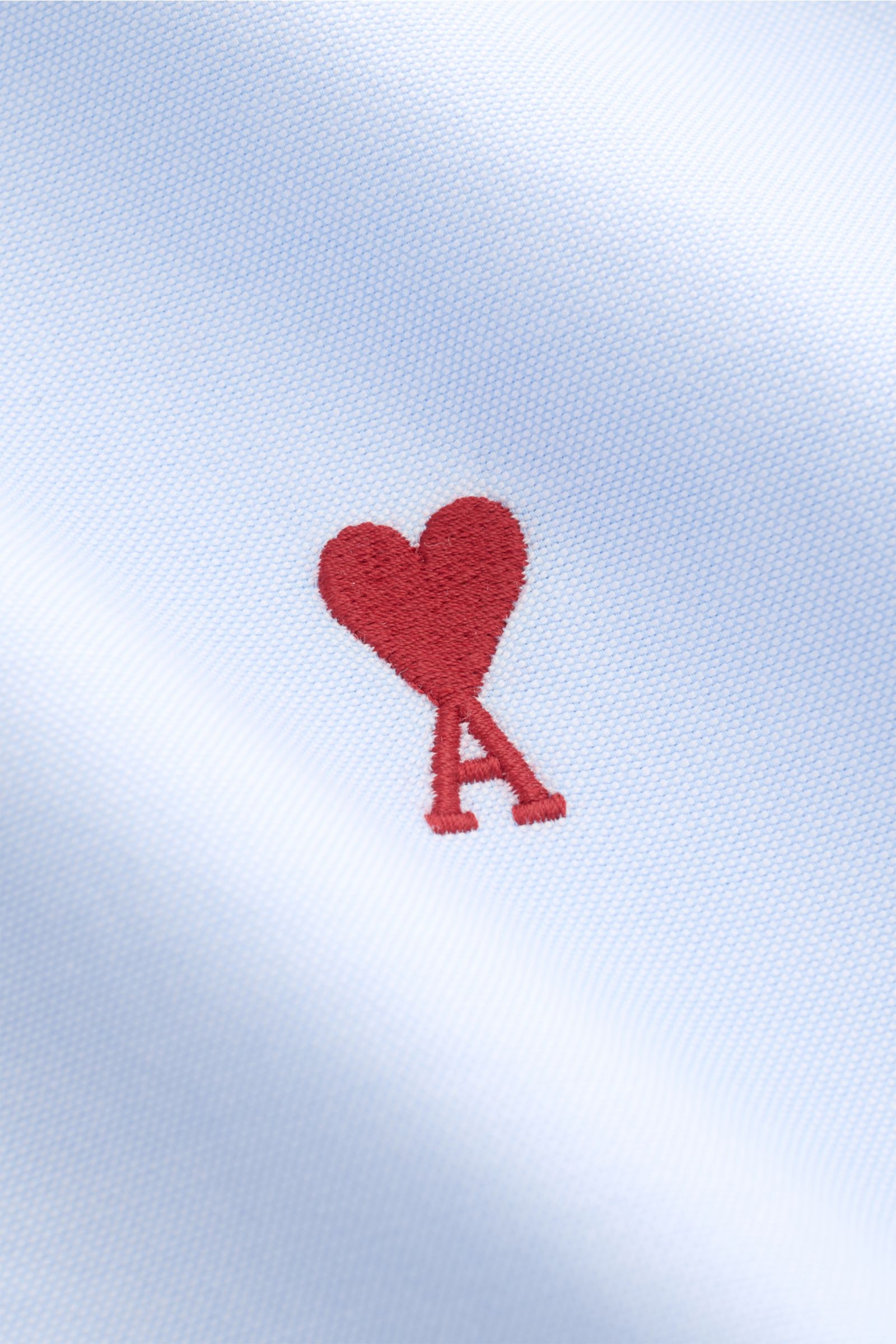 Close-up front view of Ami Paris Oxford shirt button-down collar light blue showing signature red heart stitching on pure cotton Oxford fabric.

For relaxed casual styles and more formal looks: This elegant shirt from AMI PARIS with signature heart sti