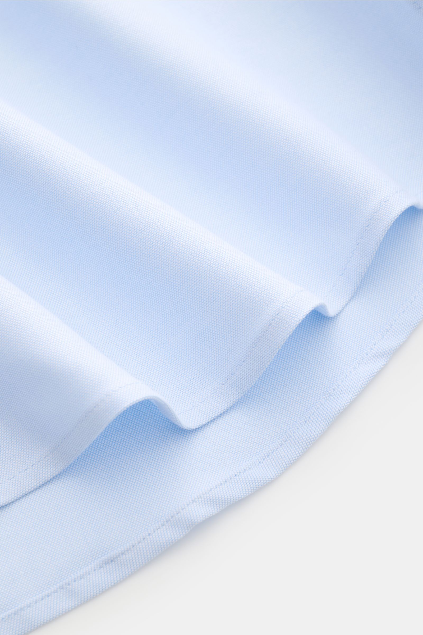 Close-up of light blue Ami Paris Oxford shirt button-down collar showing pure cotton Oxford fabric texture and rounded hem from a side angle. For relaxed casual styles and more formal looks: This elegant shirt from AMI PARIS with signature heart stitching