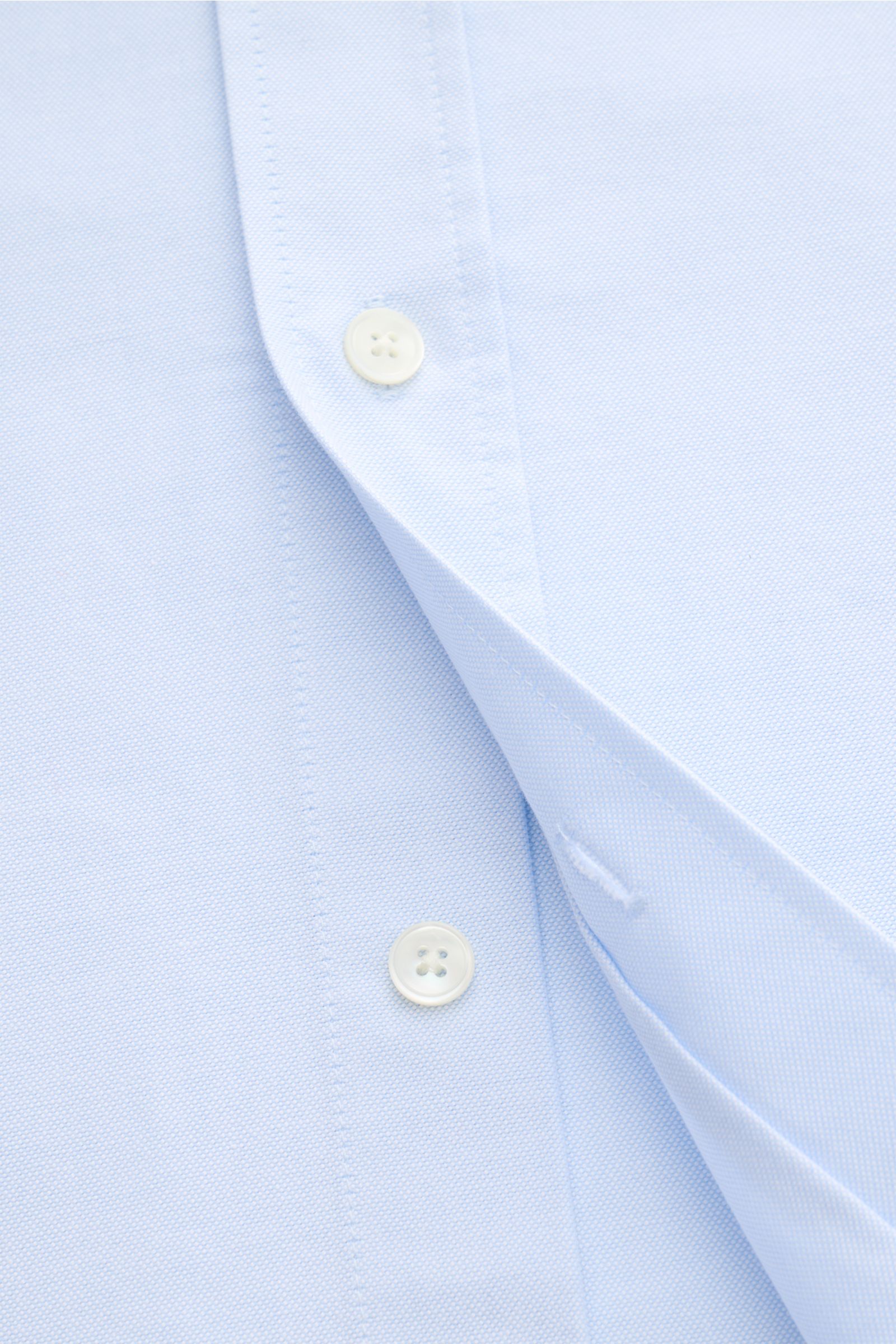 Close-up front view of Ami Paris Oxford shirt button-down collar light blue showing patch button placket with mother-of-pearl buttons and fine Oxford cotton fabric texture. For relaxed casual styles and more formal looks: This elegant shirt from AMI PARIS