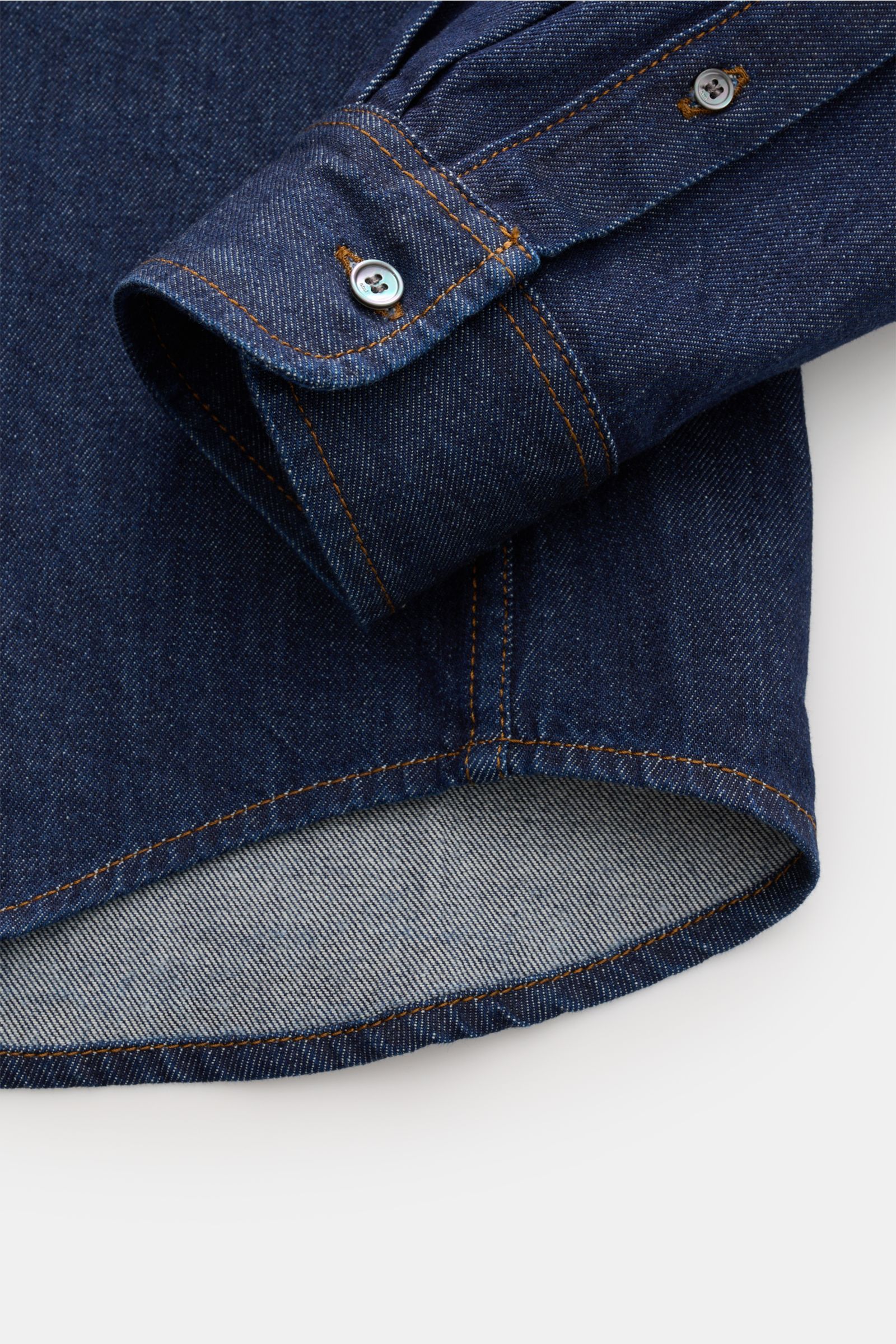 Nahaufnahme des Ärmels und Saums vom Ami Paris Jeanshemd Button-Down-Kragen navy aus reinem Baumwoll-Denim mit Oversized Fit, Sportmanschette und gerundetem Saum, fotografiert von schräg oben.