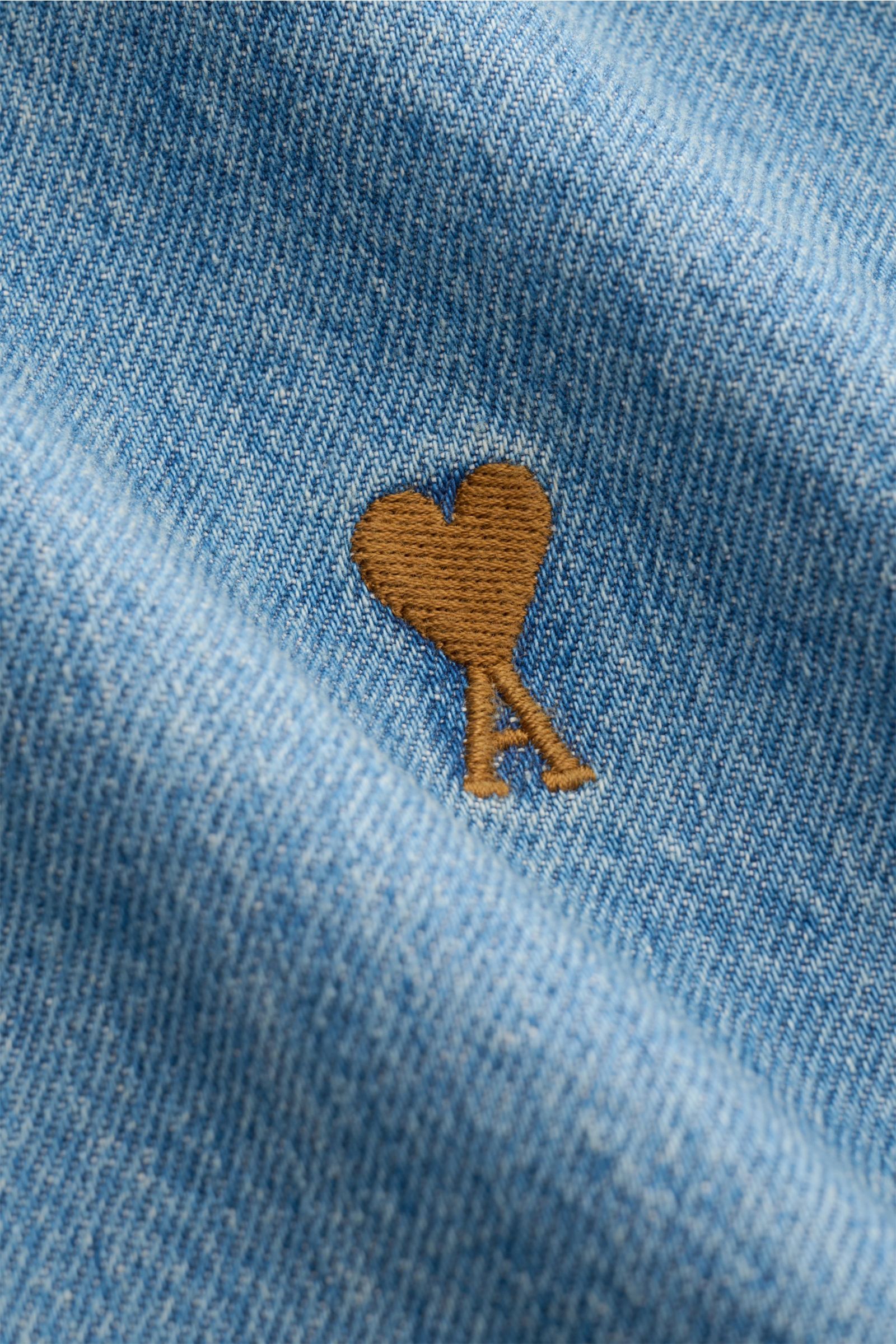 Nahaufnahme des Ami Paris Jeanshemd Button-Down-Kragen rauchblau in leichter Stofffalte mit brauner Herz-A-Logo-Stickerei auf reiner Baumwolle.