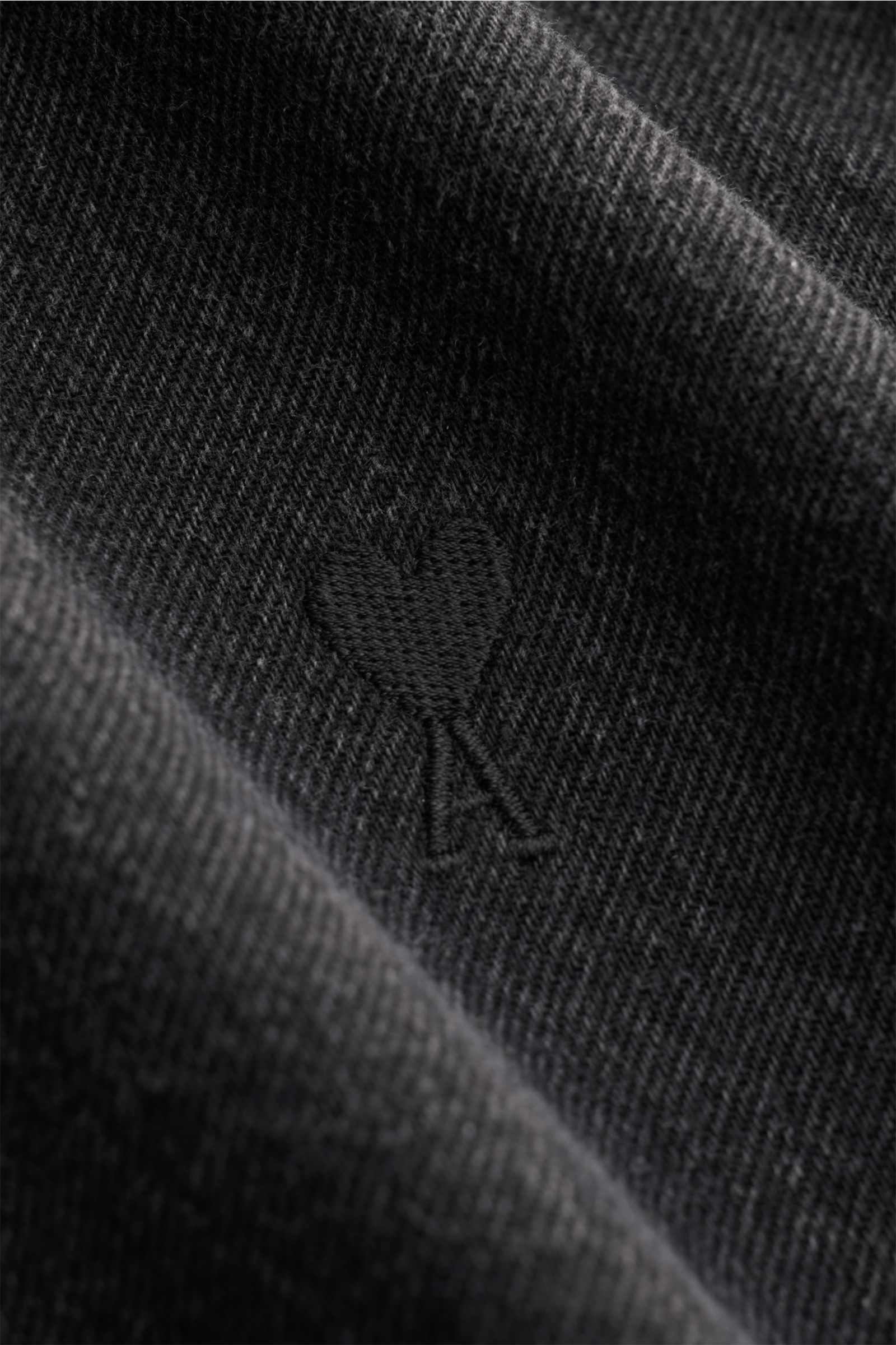 Nahaufnahme des markentypischen Stickherzens auf dem dunklen Denimstoff des Ami Paris Jeanshemds Button-Down-Kragen dunkelgrau aus reiner Baumwolle.