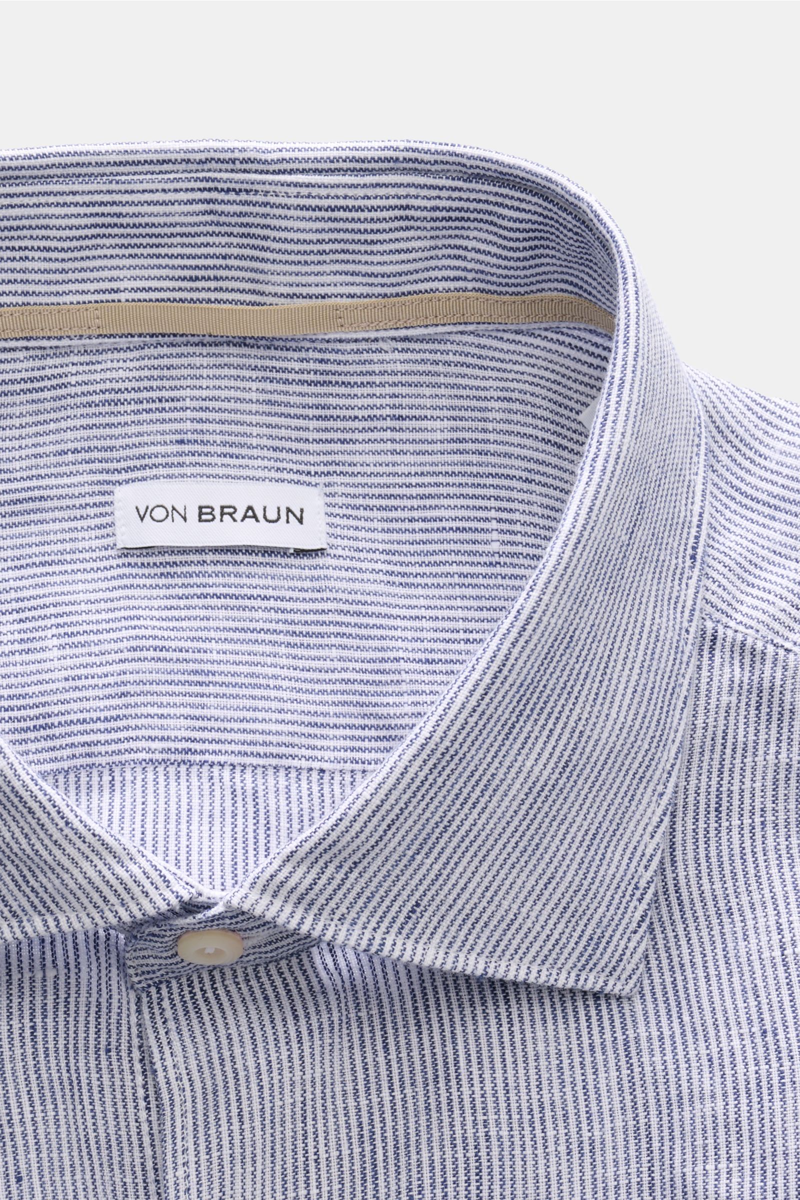 Nahaufnahme von von Braun Leinenhemd Haifisch-Kragen navy/weiß gestreift, fotografiert von oben, reine Leinenqualität mit feinem Streifenmuster.