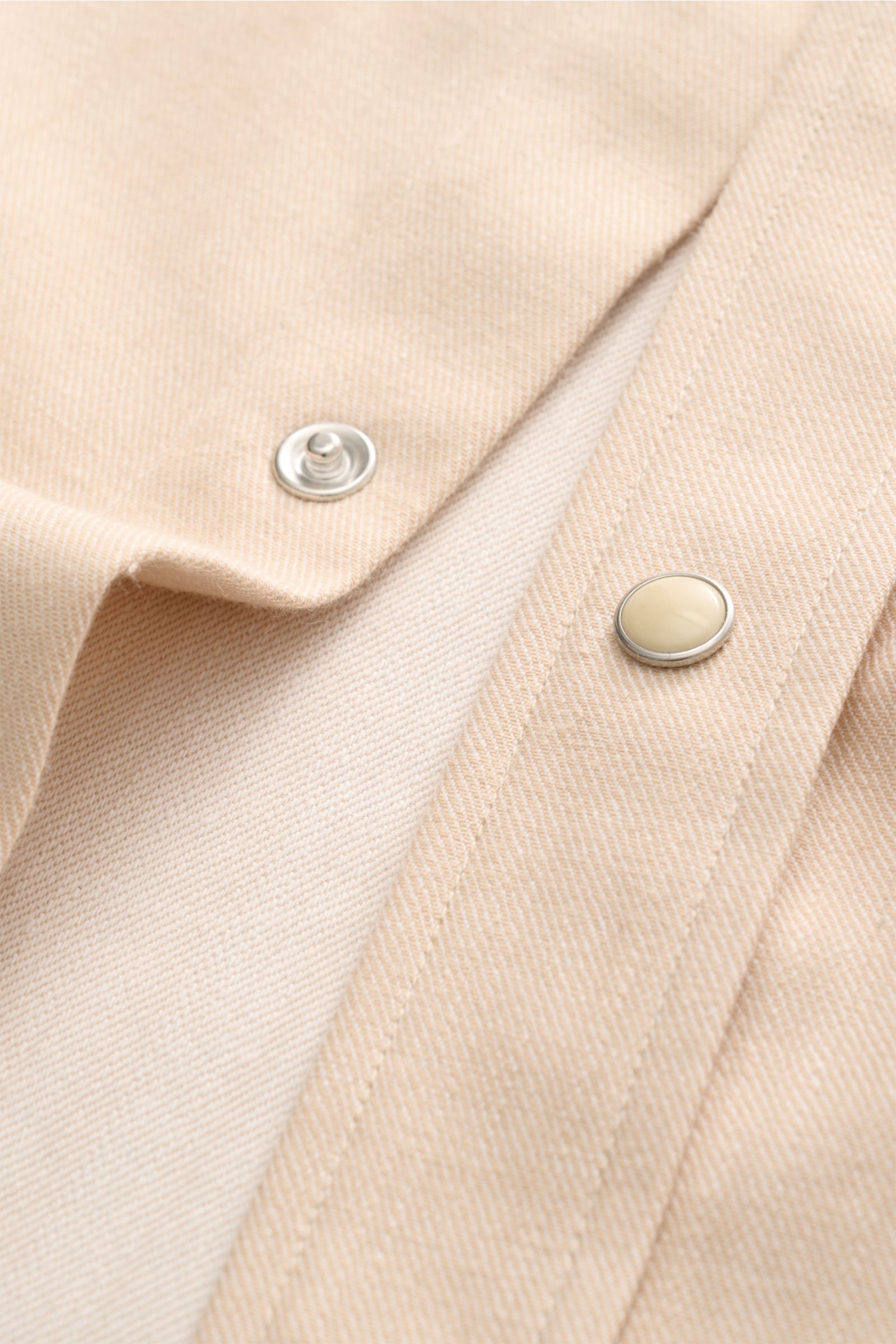 Nahaufnahme des Doppiaa Jeanshemds 'Aariosto' Kent-Kragen sand mit weichem, elastischem Baumwoll-Denim und Perlmutt-Druckknöpfen, fotografiert von schräg oben.