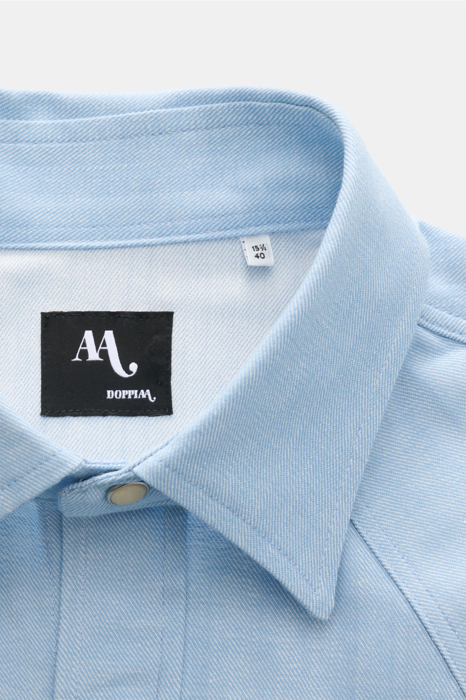 Doppiaa Jeanshemd 'Aariosto' Kent-Kragen hellblau aus weichem Denim, Detailaufnahme von oben mit Perlmutt-Druckknopf und Markenlabel.