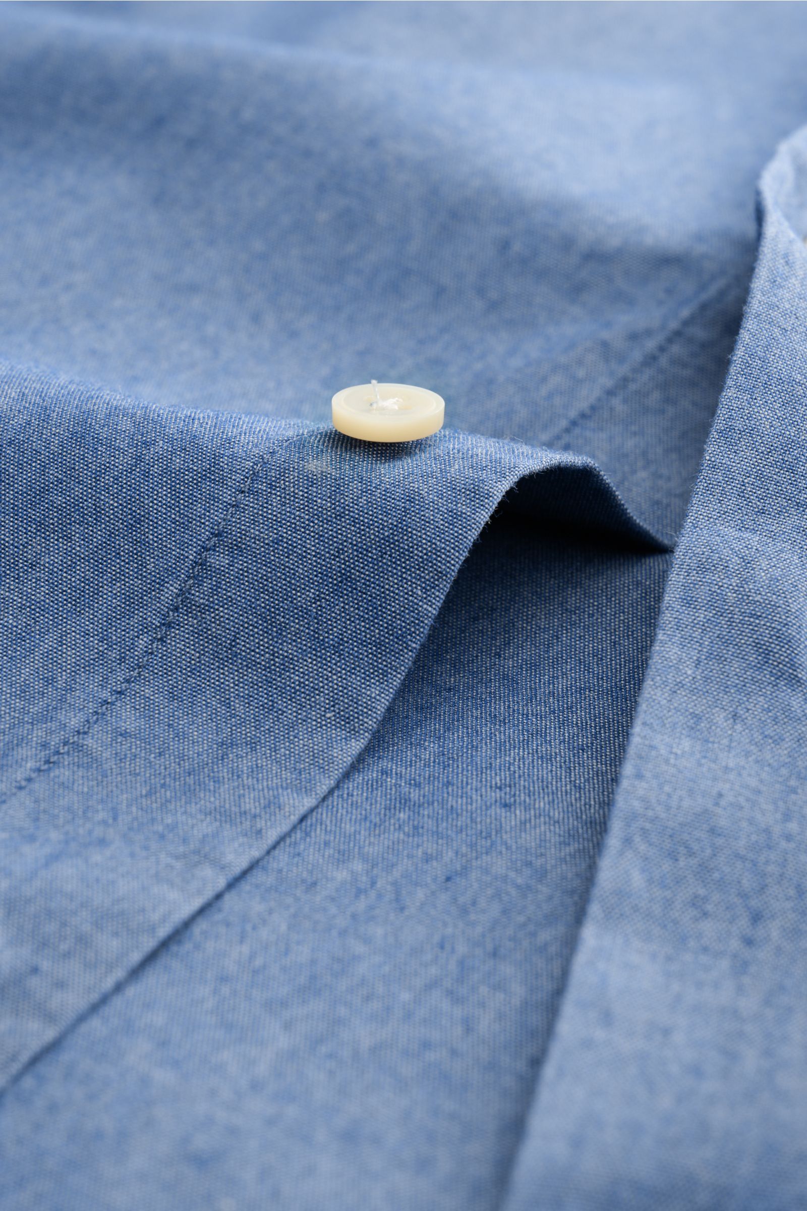 Guglielminotti Chambray shirt shark collar smoky blue shown in close-up from a top angle focusing on pure cotton fabric texture and a cream button.