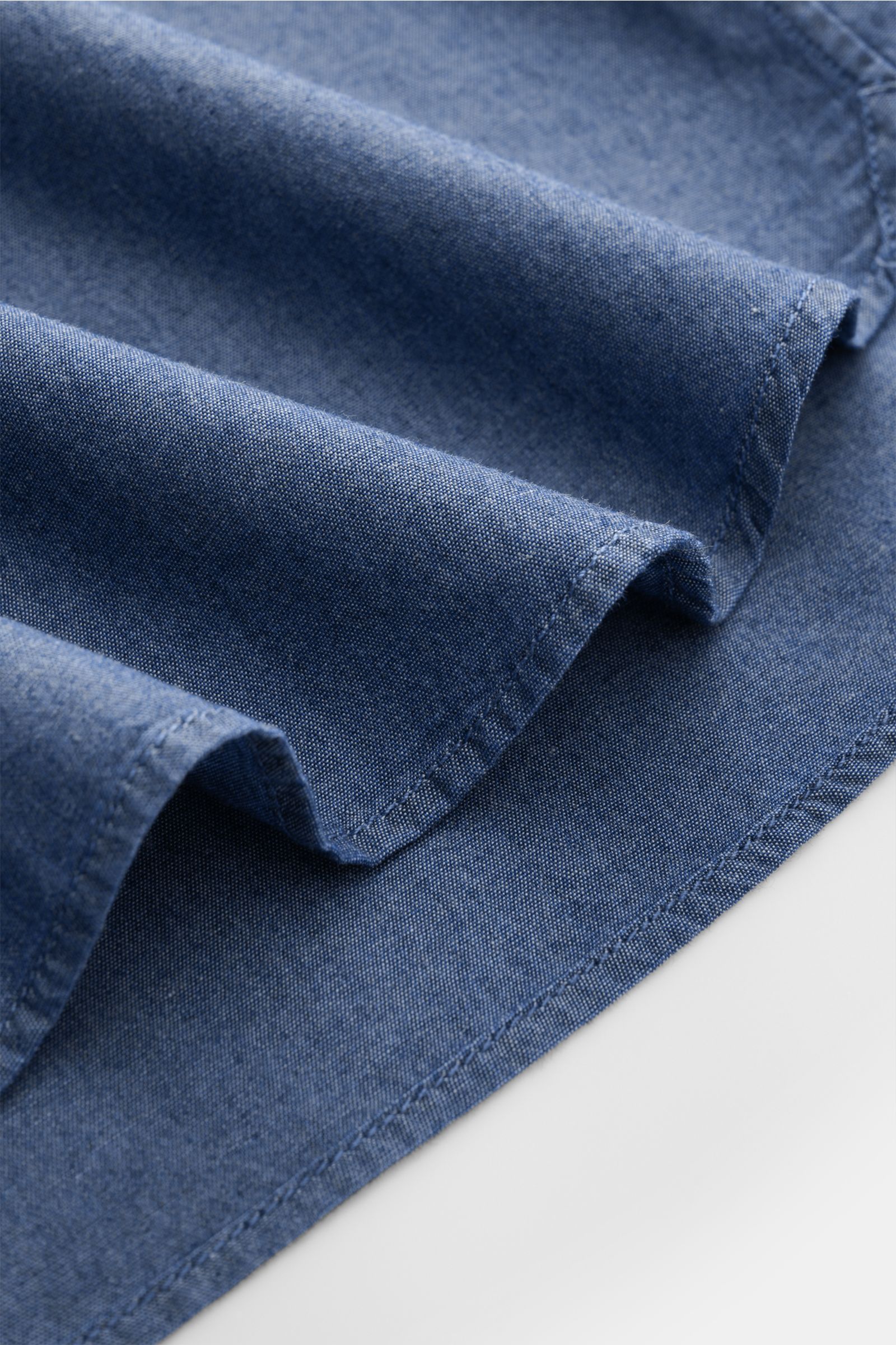 Guglielminotti Chambray shirt shark collar dark blue shown in close-up from a side angle, highlighting pure cotton fabric, smooth feel, oversized fit, shark collar, patch breast pockets, patch button placket, classic barrel cuffs, and a slightly rounded h