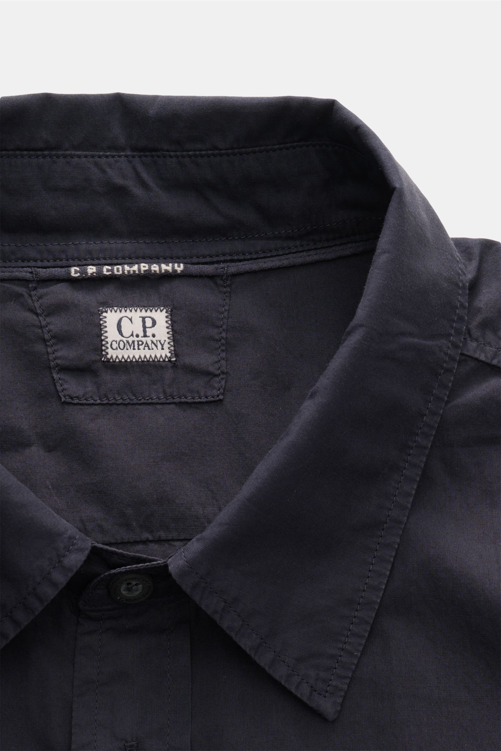 Nahaufnahme des C.P. Company Casual Hemd schmaler Kragen navy, fotografiert von oben auf den Kragen und das Logo aus reiner Baumwolle.