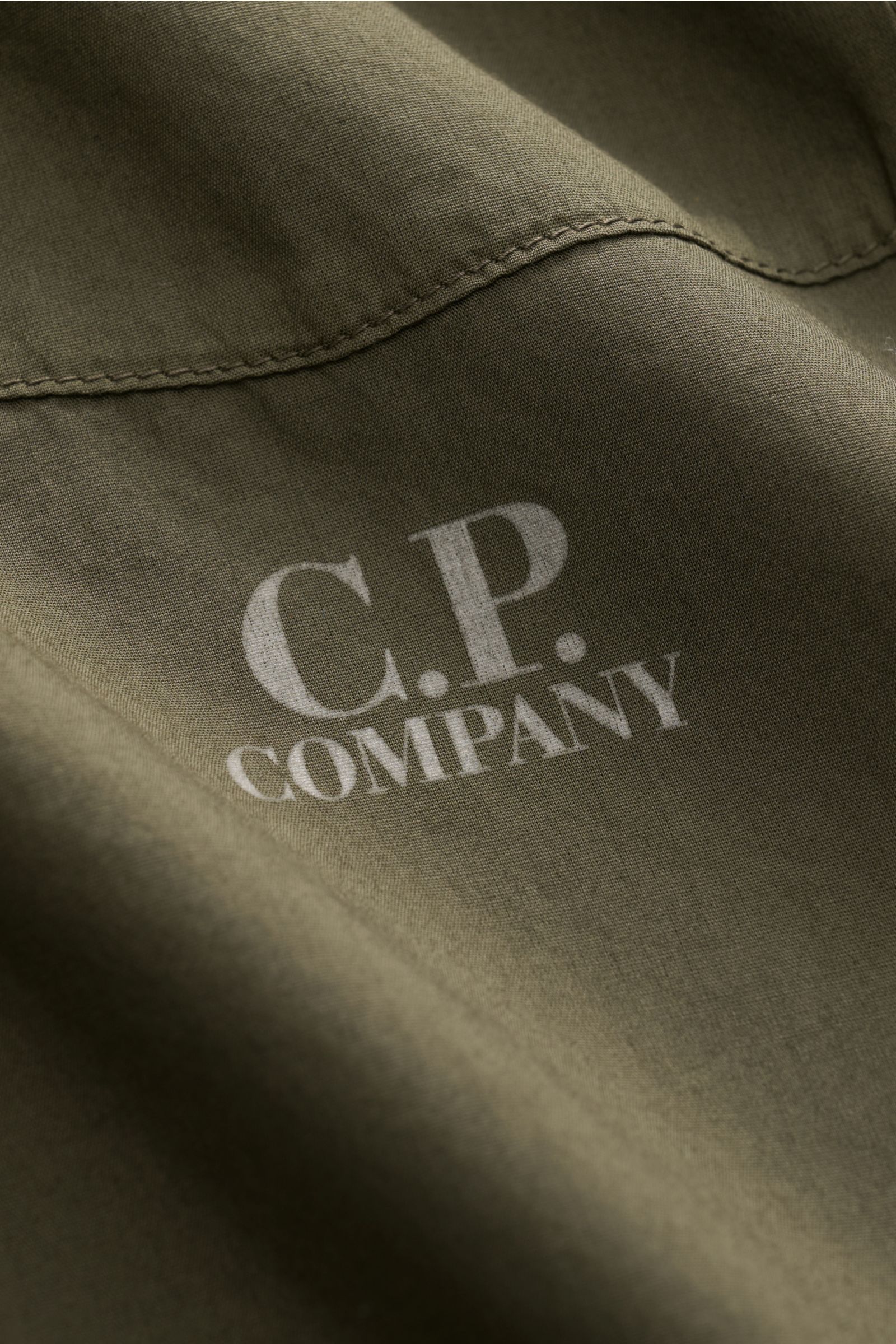 Nahaufnahme des C.P. Company Casual Hemds schmaler Kragen dark olive aus reiner Baumwolle, garment dyed, mit Logo-Print, weichem Griff.