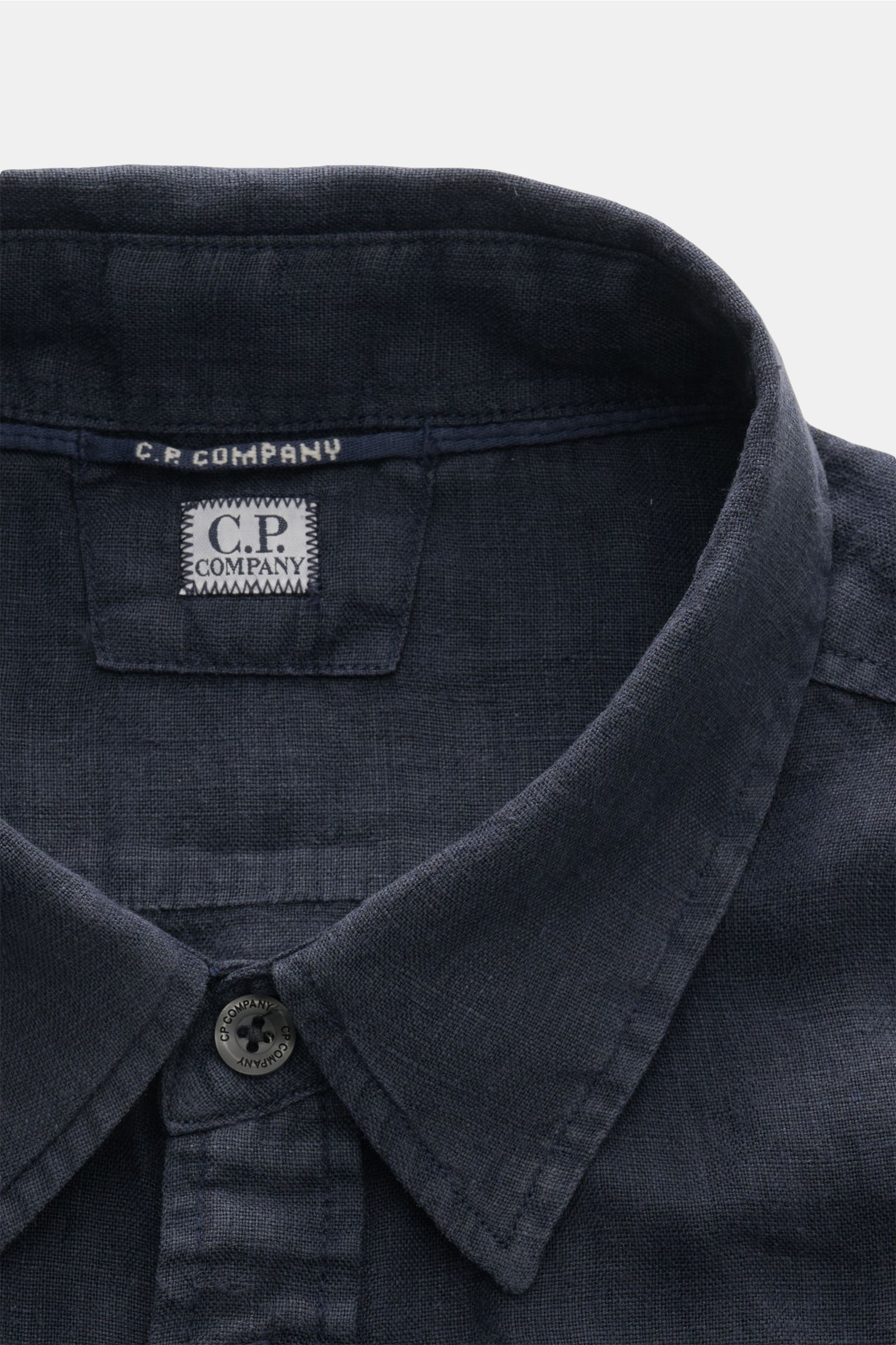 Close-up front view of the C.P. Company Linen shirt slim collar navy, showing the narrow collar, top button, and C.P. Company label inside. 