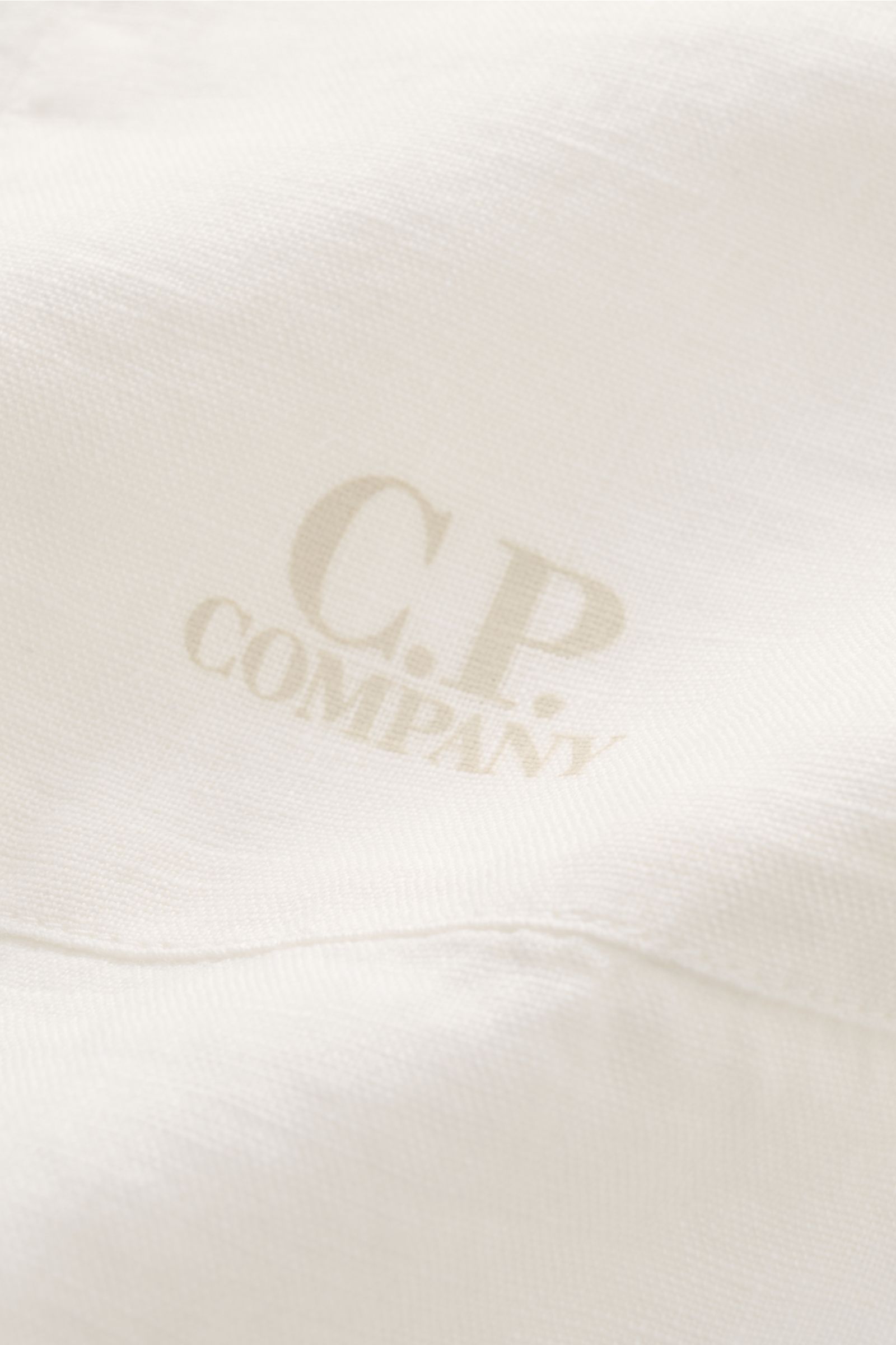 C.P. Company Linen shirt slim collar off-white shown in close-up from above, highlighting pure linen fabric, soft feel, garment-dyed texture, and subtle logo print on pocket section. 