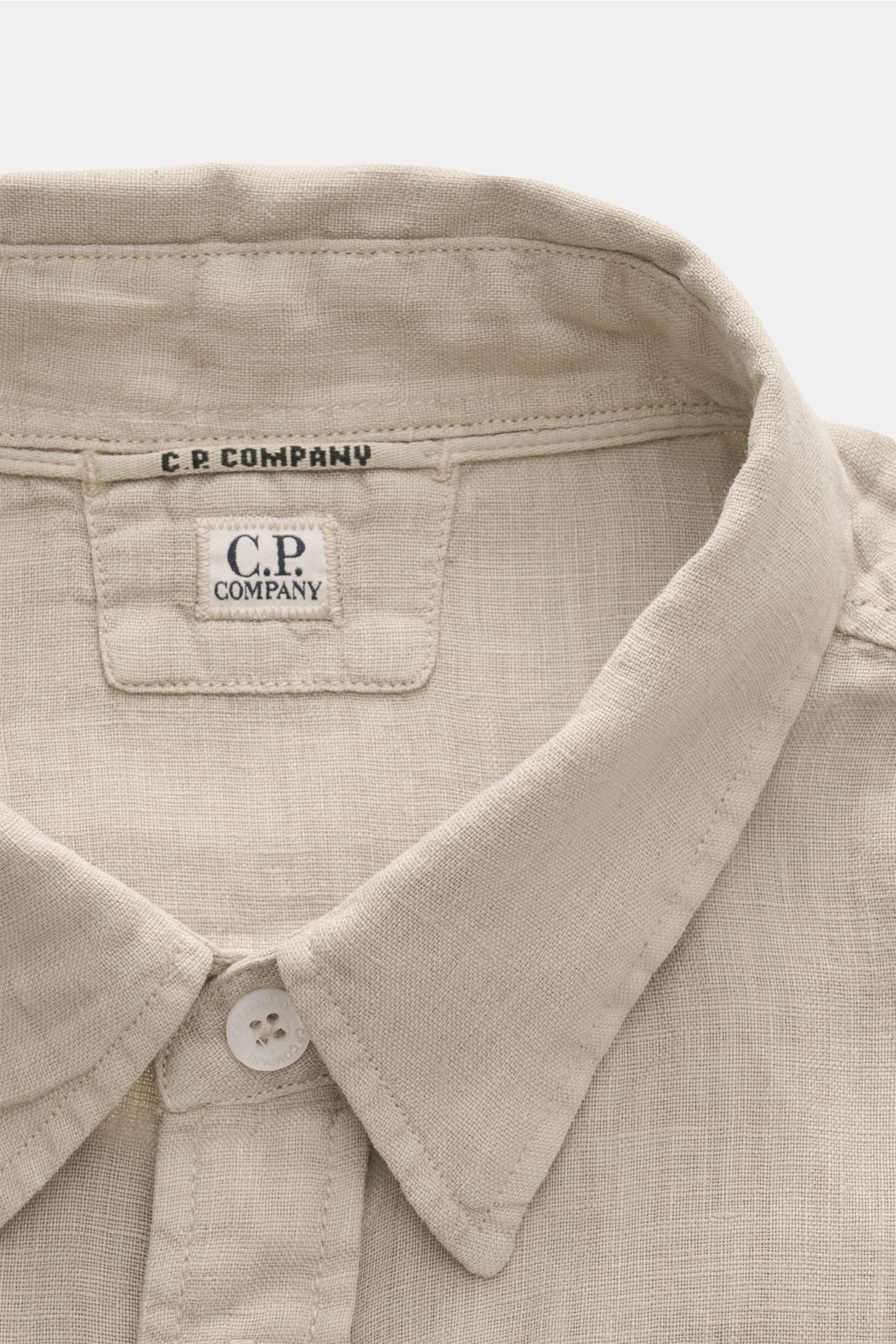 Close-up front top view of C.P. Company Linen shirt narrow collar sand, showing narrow collar, patch button placket, and linen texture. 