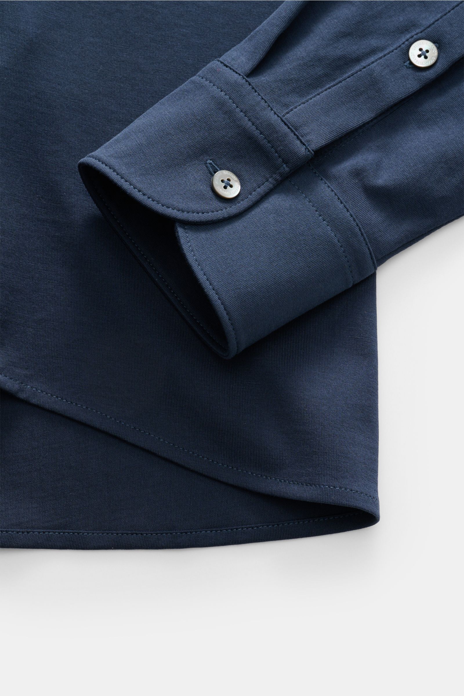 Close-up view of the cuff and hem of the Stefan Brandt Jersey-Hemd 'Otis' Haifisch-Kragen dunkelblau, showing soft, smooth dark blue Pima cotton jersey fabric, classic sport cuff with button, extra slim fit, French button placket, and rounded hem. Flexibl