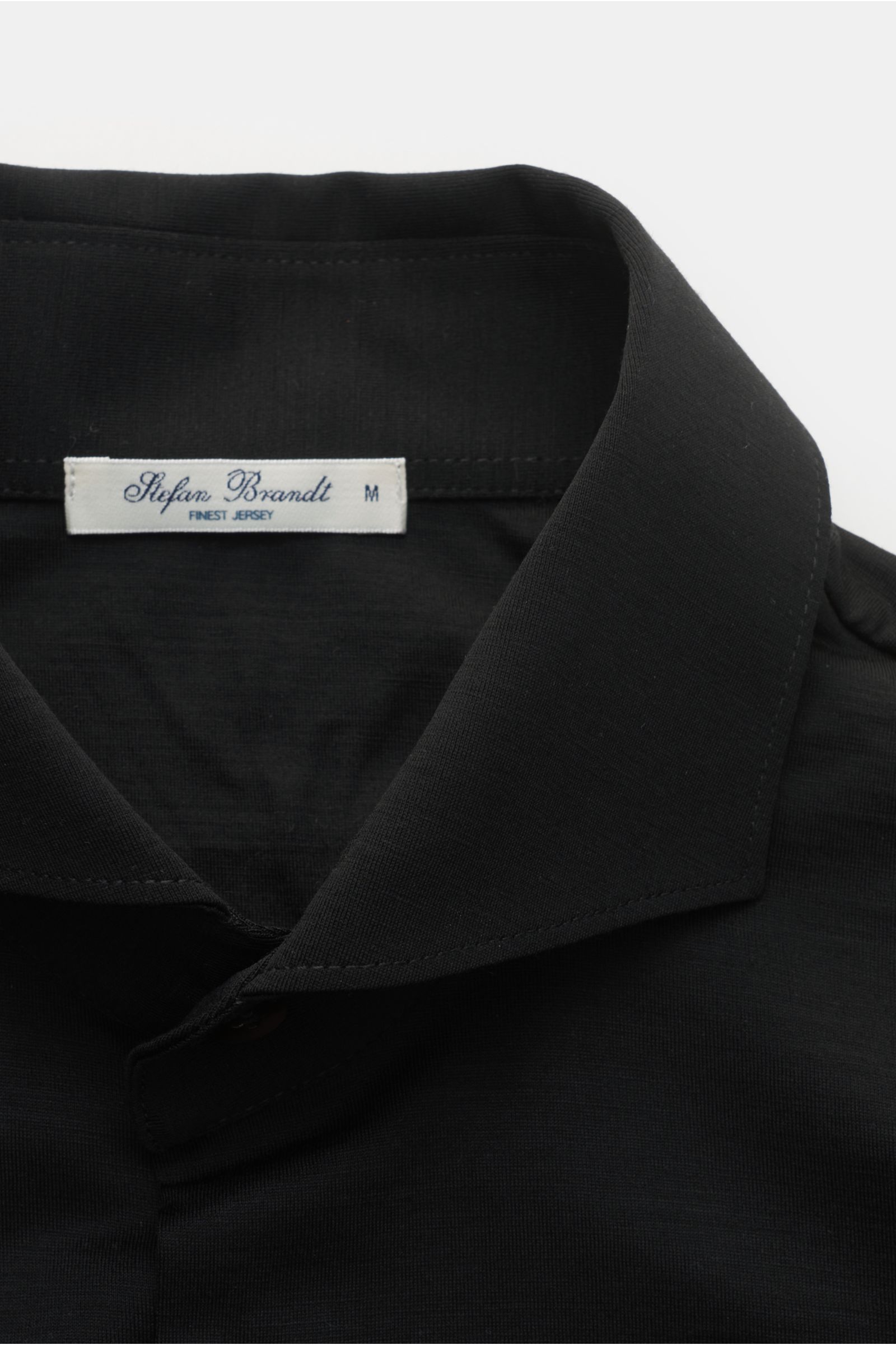 Nahaufnahme von Stefan Brandt Jersey-Hemd 'Otis' Haifisch-Kragen schwarz, flexibler Pima-Baumwoll-Jersey, glatter Griff, Haifisch-Kragen, französische Knopfleiste.