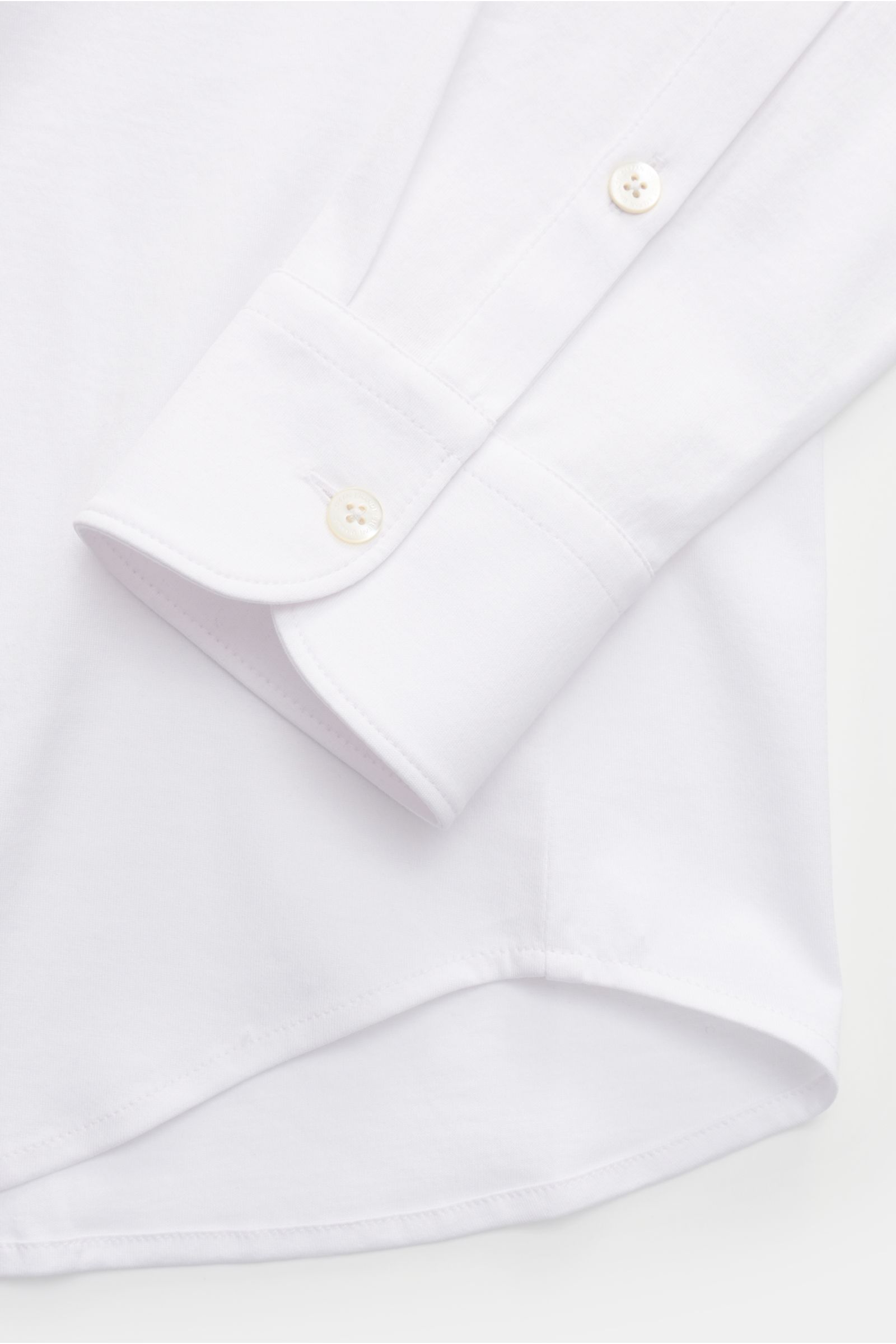 Close-up image of the sleeve and rounded hem of the Stefan Brandt Jersey-Hemd 'Otis' Haifisch-Kragen weiß, photographed from above, showing its flexible, smooth pure Pima cotton jersey fabric, extra slim fit, shark collar, French button placket, classic s