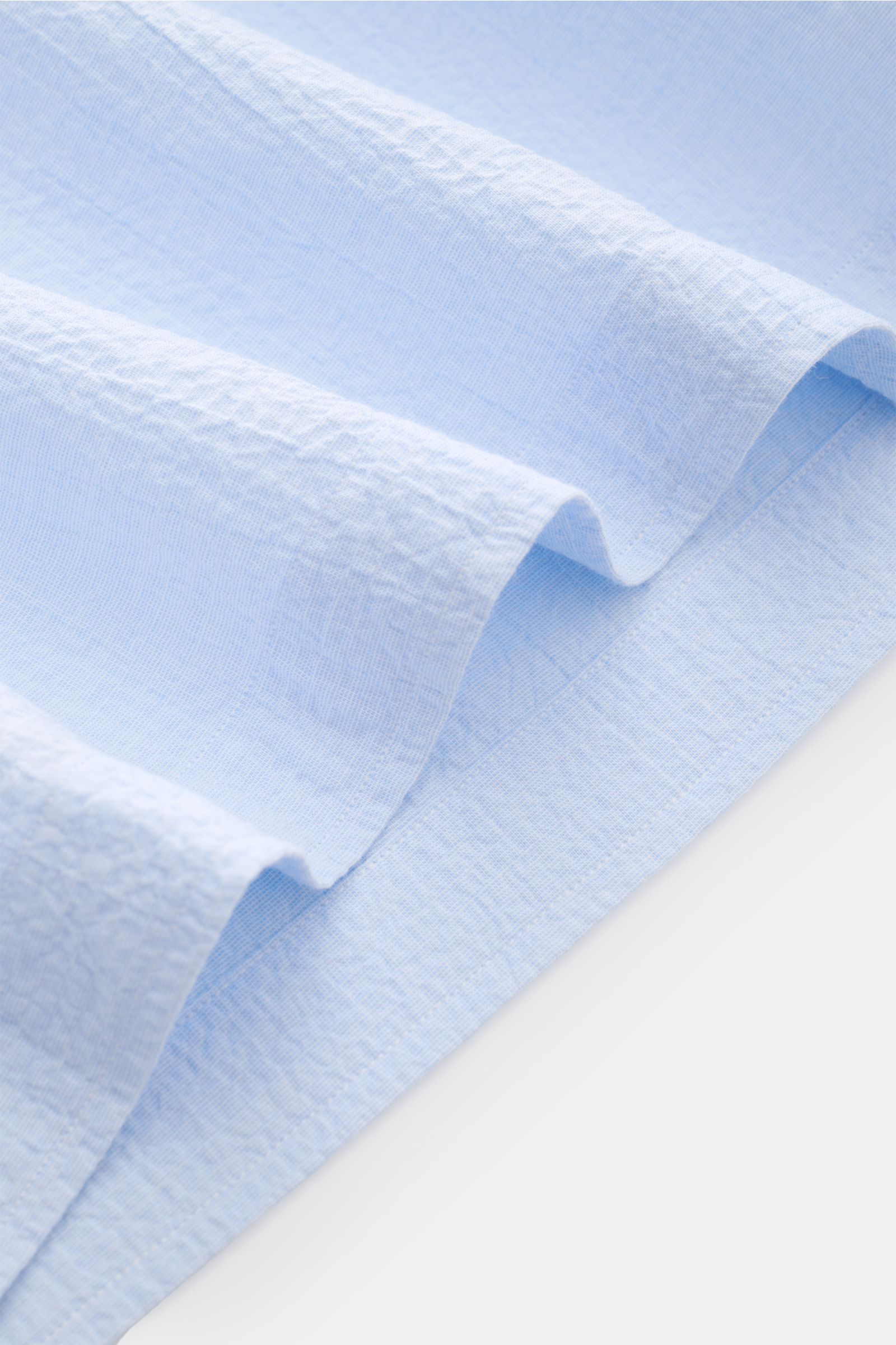 Nahaufnahme des Giampaolo Seersucker Popover-Hemd Haifisch-Kragen hellblau, Detail der elastischen Baumwolle mit strukturierter Seersucker-Oberfläche und geradem Saum, fotografiert aus schräger Perspektive.
