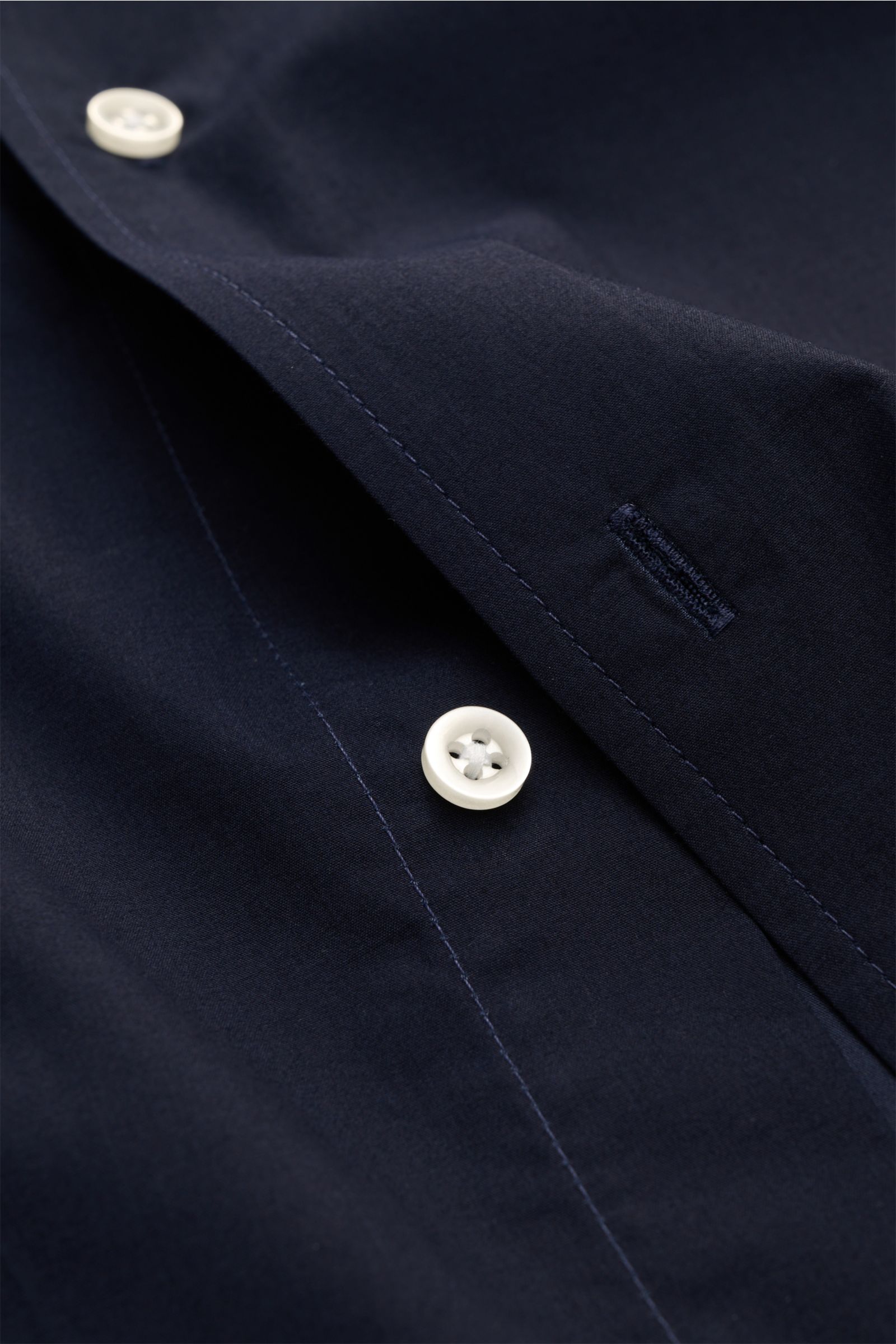 Nahaufnahme des Officine Générale Casual Hemd 'Jahlan' Grandad-Kragen navy aus Baumwoll-Popeline mit weichem Griff, Regular Fit, französischer Knopfleiste und schmaler Sportmanschette, fotografiert von schräger Perspektive.